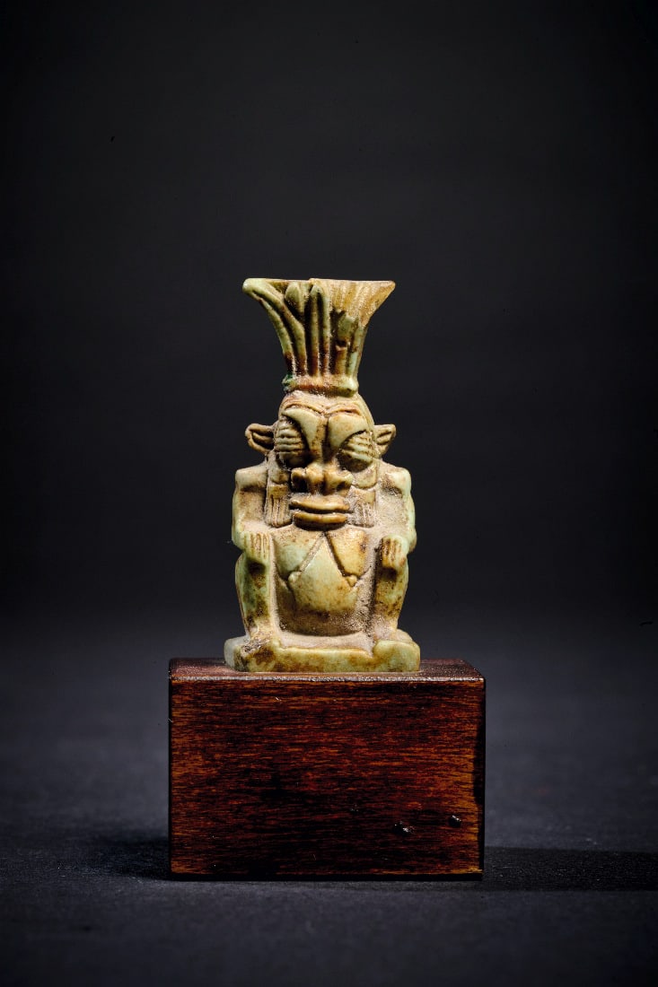 Amulett des Bes.: Amulett des Bes. Spaetzeit, 1. Jt. v. Chr. H 5,2cm (mit Sockel), H 3,5cm (ohne Sockel). Aus hellgruener Fayence. Hockende Zwergengestalt mit Federkrone an durchbohrtem Rueckenpfeiler. Intakt.
