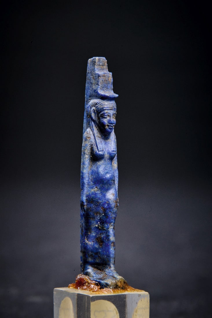 Amulett der Isis.: Amulett der Isis. Neues Reich, 1550 - 1070 v. Chr. H 5,4cm (mit Sockel), H 4cm (ohne Sockel). Aus Lapislazuli. Stehende, nackte weibliche Figur mit Krone an Rueckenpfeiler. Mit Bohrung. Intakt.