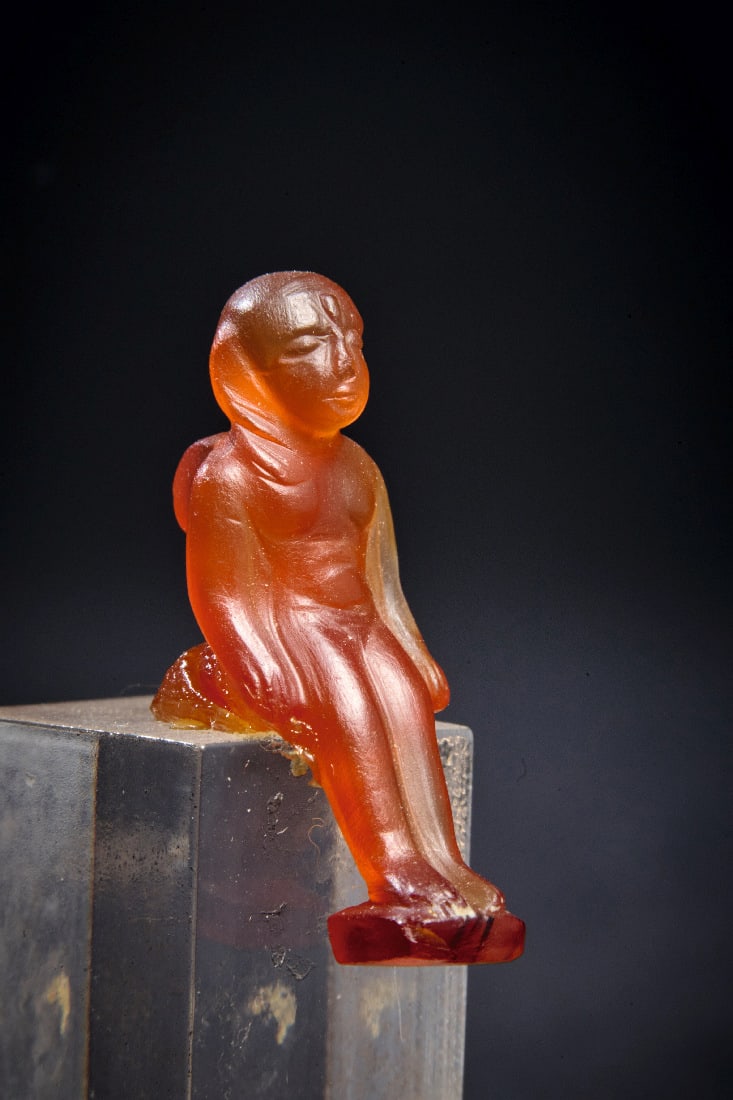Amulett des Horuskindes.: Amulett des Horuskindes. Spaetzeit, 664 - 332 v. Chr. H 4cm (mit Sockel), H 2,2cm (ohne Sockel). Aus Karneol. Sitzender, nackter Knabe mit Jugendlocke. Auf dem Ruecken oese. Unter den Fuessen