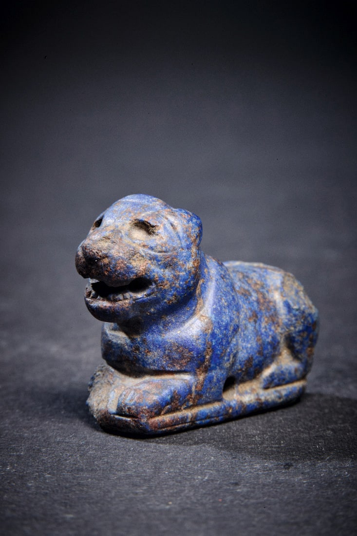Spielstein oder Amulett in Form eines kauernden Loewen.: Spielstein oder Amulett in Form eines kauernden Loewen. Praedynastisch - Altes Reich, ca. 3000 - 2300 v. Chr. L 3cm. Auf rechteckiger Platte liegender Loewe aus Lapislazuli mit aufgerissenem Maul.