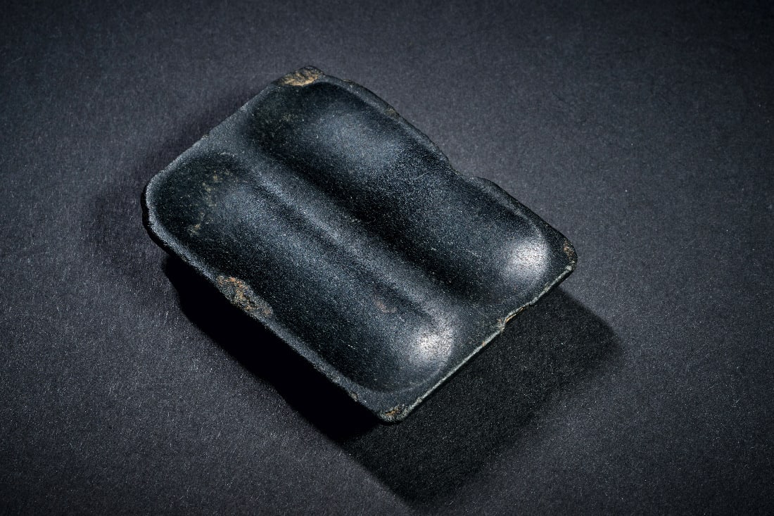 Schminkpalette.: Schminkpalette. Ptolemaeerzeit, ca. 323 - 30 v. Chr. Schwarzer Steatit. L 6,5cm B 5cm H 1,2cm. Oben mit zwei laengsovalen Vertiefungen. Seitlich mit schoenem Doppelprofil. An den Raendern bestossen.