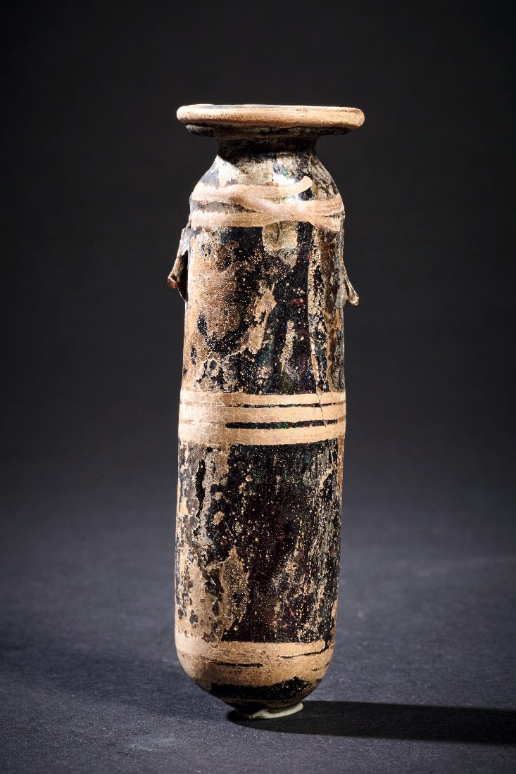 Seltenes Alabastron in Sandkerntechnik mit weissem Liniendekor.: Seltenes Alabastron in Sandkerntechnik mit weissem Liniendekor. oestliches Mittelmeergebiet, 6. - 4. Jh. v. Chr. H 11,7cm. Dunkelbraun, stark korrodiertes Glas. Schlankes Gefaess mit breit