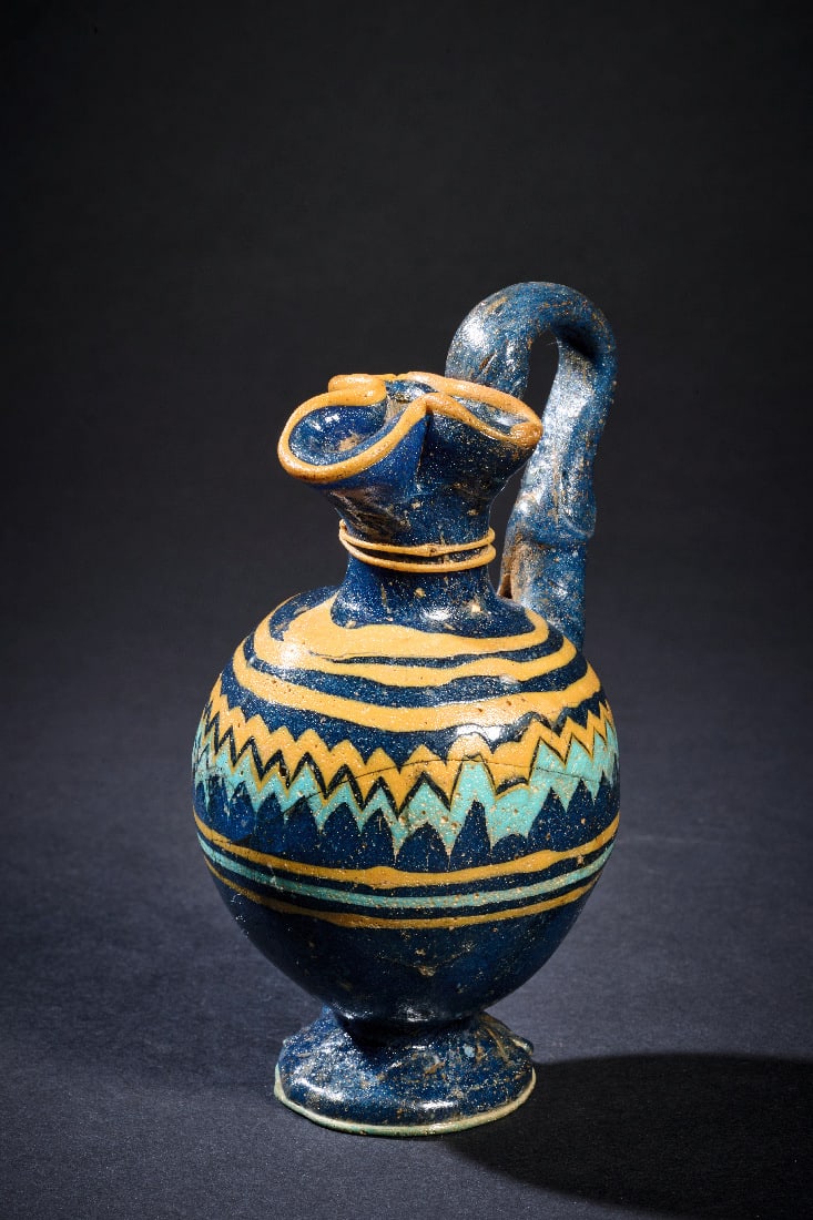 Grosse Oinochoe mit polychromem Fadendekor.: Grosse Oinochoe mit polychromem Fadendekor. oestliches Mittelmeergebiet, 6. - 4. Jh. v. Chr. H 11,7cm. Tiefblaues, transluzides Glas. Sandkerntechnik. Bikonischer, leicht gedrungener Koerper auf ausge