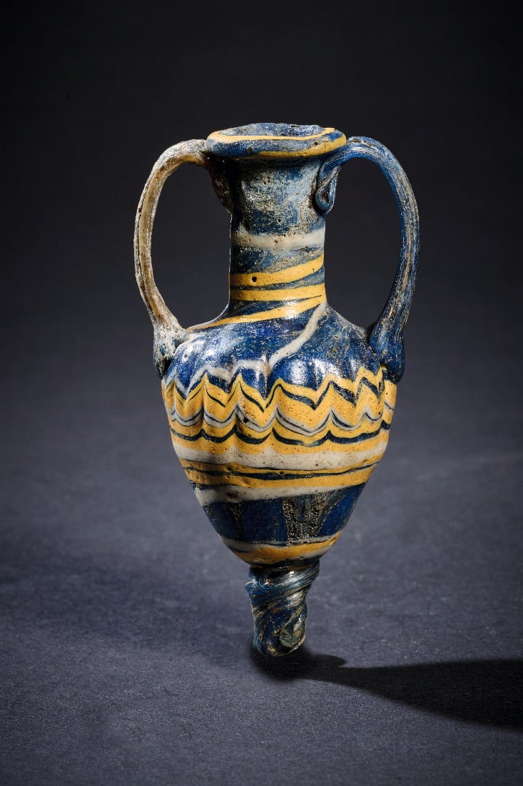 Fein dekorierter Amphoriskos mit Zickzackband.: Fein dekorierter Amphoriskos mit Zickzackband. Mittelmeergebiet, 2. - 1. Jh. v. Chr. H 8cm. Tiefes mattblaues Glas. Sandkerntechnik. Kleines, elegant proportioniertes Gefaess mit schlankem Hals und