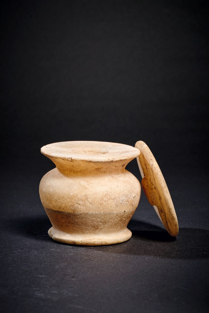 Massives Salbgefaess mit Deckel aus Alabaster.: Massives Salbgefaess mit Deckel aus Alabaster. Neues Reich, 18. Dynastie, 1550 - 1292 v. Chr. H mit Deckel 7,1cm, ? 6,8cm. Leicht geaederter Alabaster. Konischer Koerper mit abgerundeter Schulter und 