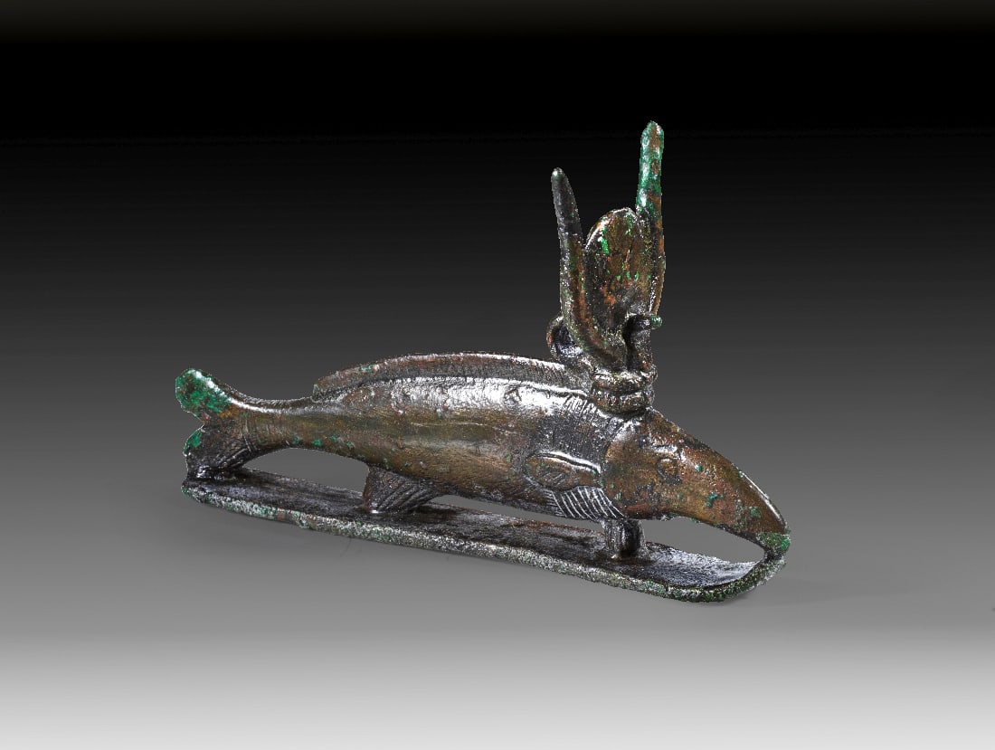 Oxyrhynchos-Fisch.: Oxyrhynchos-Fisch. Spaetzeit, 1. Jt. v. Chr. L 13cm, H 8cm. Bronzevollguss. Nilhecht mit Kuhgehoern, Sonnenscheibe und Uraeus auf einem "Schlitten". Gruenbraune Patina, intakt. Provenienz: Ex Slg. Dr.