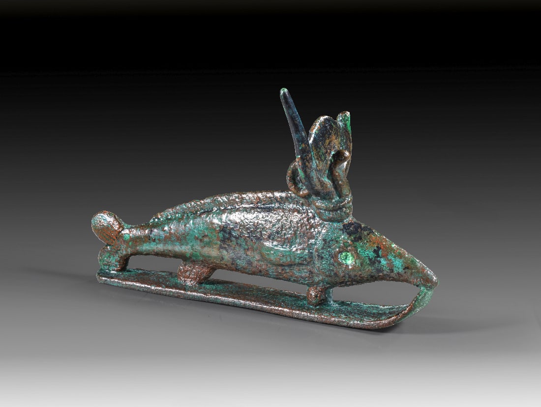 Oxyrhynchos-Fisch.: Oxyrhynchos-Fisch. Spaetzeit, 1. Jt. v. Chr. L 13cm, H 8,2cm. Bronzevollguss. Nilhecht mit Kuhgehoern, Sonnenscheibe und Uraeus auf einem "Schlitten". Gruenbraune Patina, Einlagen der Augen fehlen, Sp