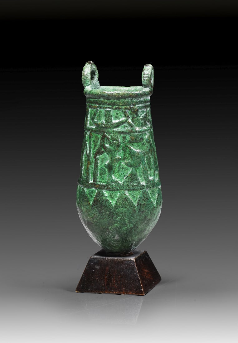 Bronze-Situla mit Reliefdekor.: Bronze-Situla mit Reliefdekor. Ptolemaeisch, ca. 305 - 30 v. Chr. H 9cm, mit Holzsockel 11cm. Bronzevollguss. Am oberen Rand zwei oesen fuer die Aufnahme des Henkels. Corpus mit zwei Registern mit fig