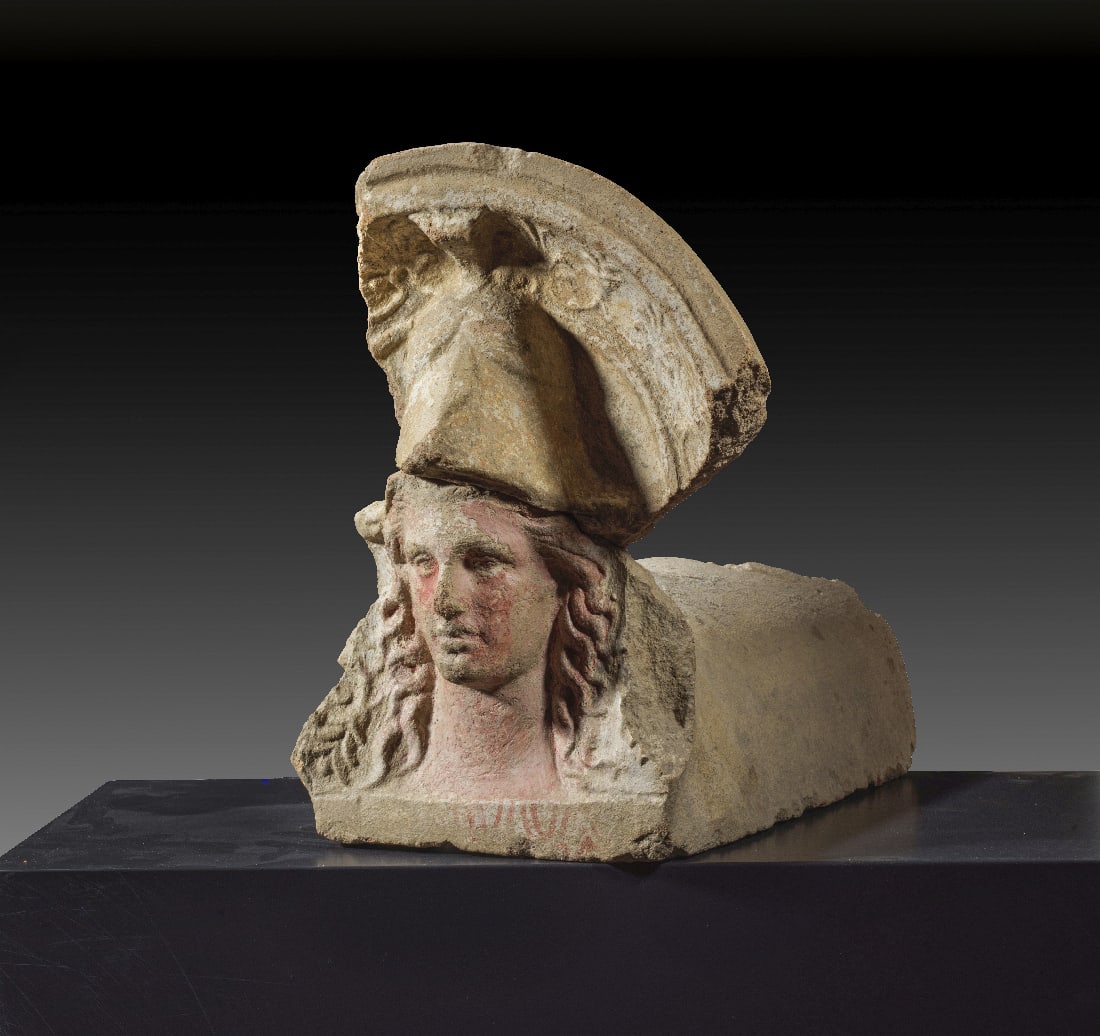 Etruskisches Antefix mit Athenakopf.: Etruskisches Antefix mit Athenakopf. 4. Jh. v. Chr. H 36,5cm, L 40cm. Rotbrauner Ton mit weisser Engobe auf der Vorderseite und Resten roter Farbe im Gesicht und in den Haaren. Dargestellt ist im halb