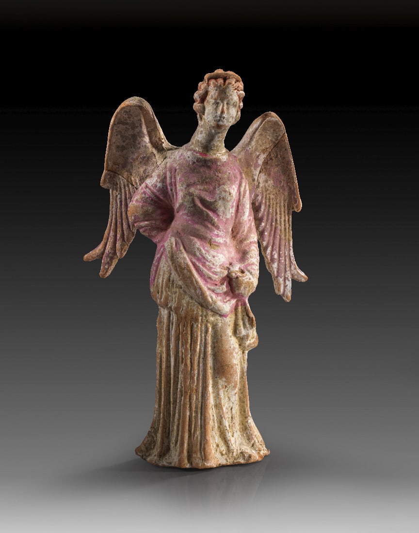 Statuette einer Nike.: Statuette einer Nike. Canosa, 3. Jh. v. Chr. H 20,5cm, B 12,5cm. Aus roetlichem Ton mit Resten von weisser Engobe und Bemalung in pink. Weibliche, gefluegelte Figur mit Melonenfrisur in Himation, die