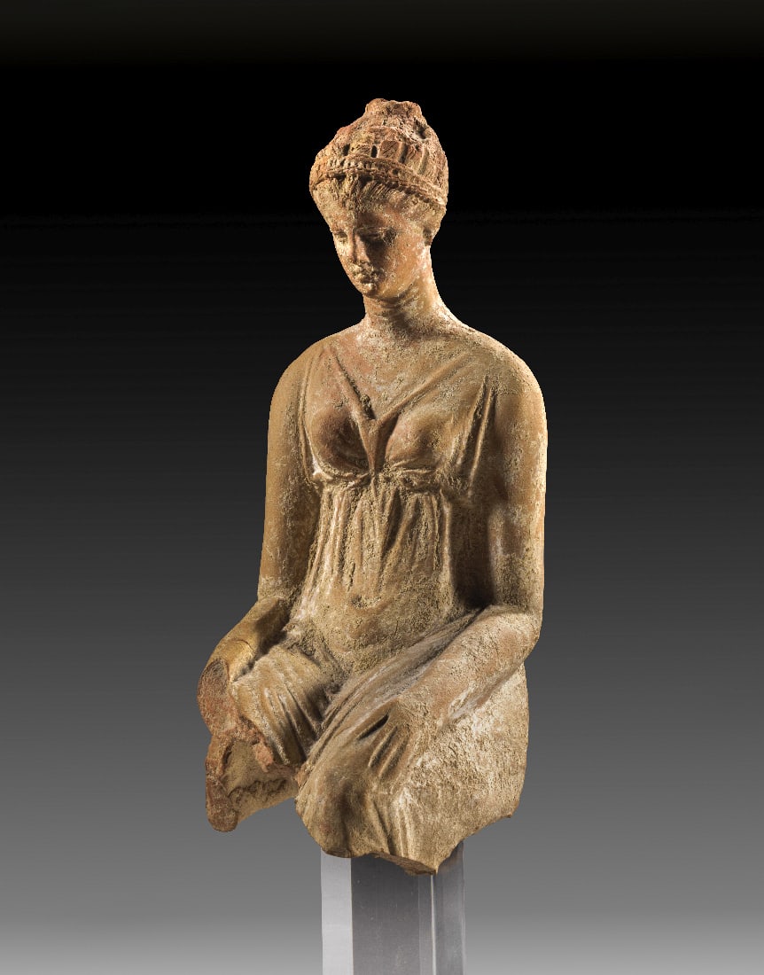 Sitzende Frauenfigur.: Sitzende Frauenfigur. Hellenistisch, 3. - 2. Jh. v. Chr. H 21cm ohne Sockel, H 30,5cm mit Sockel. Aus roetlichem Ton mit Resten von weisser Engobe. Rueckwaertig ein Brennloch. Matrizengeformt.