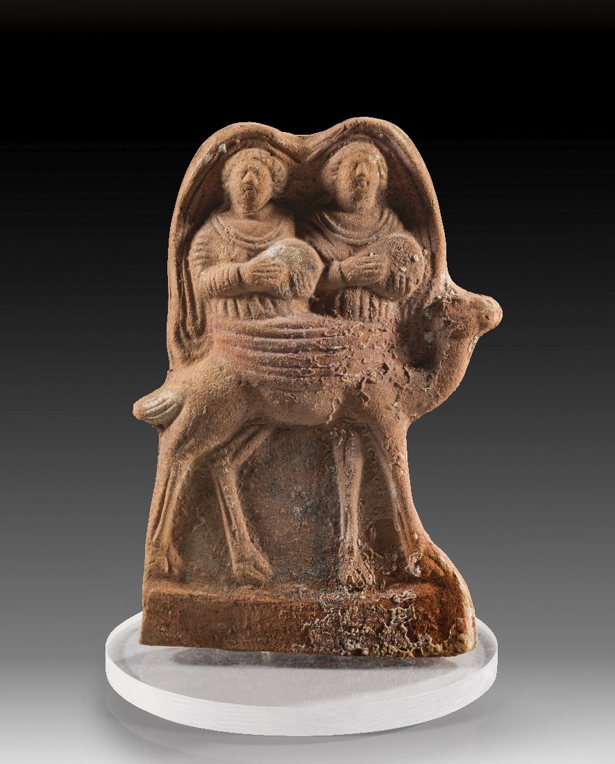 Musikantinnen auf einem Kamel.: Musikantinnen auf einem Kamel. Levante, 1. - 3. Jh. n. Chr. Hellroter Ton, H 18cm. Einseitig ausgeformte Figur mit einem nach rechts schreitenden Kamel, auf dessen Ruecken frontal zwei Frauen sitzen,