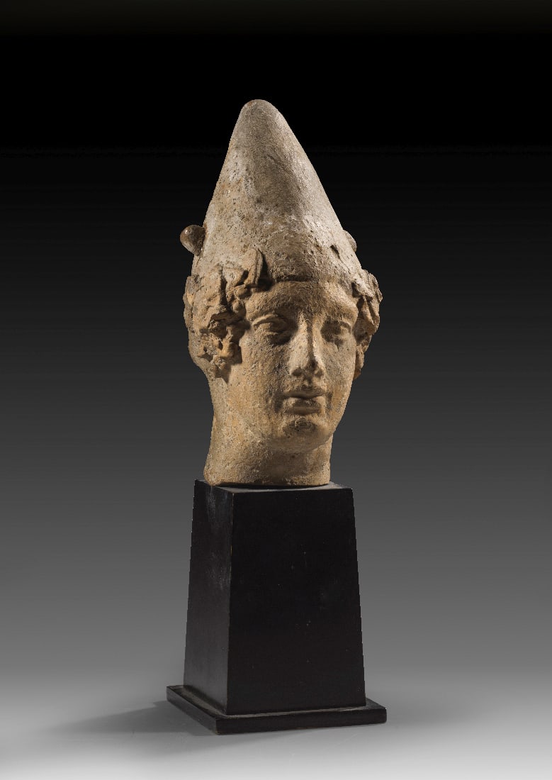 Griechischer Juenglingskopf mit Pilos.: Griechischer Juenglingskopf mit Pilos. Tarent, 4. Jh. v. Chr. H 15,2cm und mit Sockel 24,3cm. Hellbraune Terrakotta. Vorderseite aus der Matrize, Haare handgeformt, Details wie Augen und Mund in