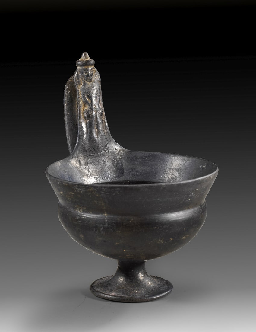 Etruskischer Kyathos aus Bucchero.: Etruskischer Kyathos aus Bucchero. 575 - 550 v. Chr. H 16,6cm, ? 12,2cm. Bucchero pesante. Halbkugeliges Becken mit hohem abgesetzten Rand auf kleinem Trompetenfuss. Seitlich ein Schlaufenhenkel,