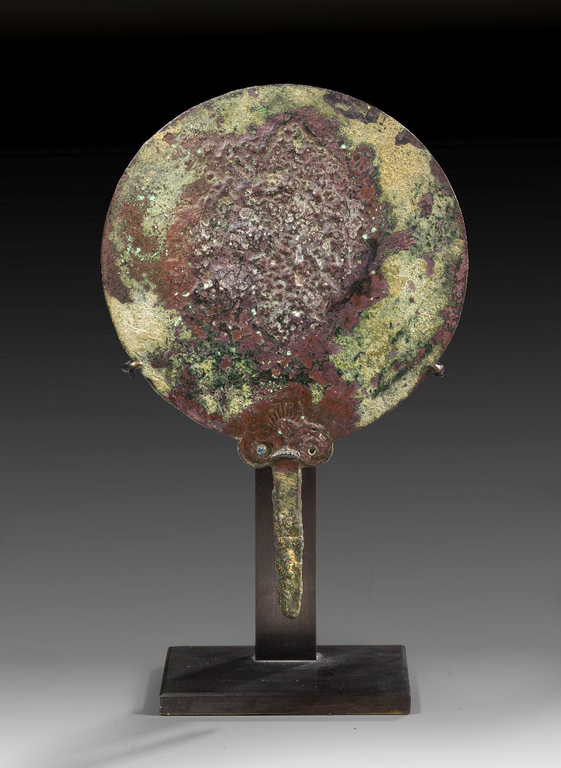 Griechischer Bronzespiegel.: Griechischer Bronzespiegel. Klassische Periode, 5. - 4. Jh. v. Chr. H 19,3cm, mit Staender 22,4cm, ? 13,2cm. Am Griffansatz schoene Palmette ueber einer Volute. Im linken Volutenherz ein blauer Glasst