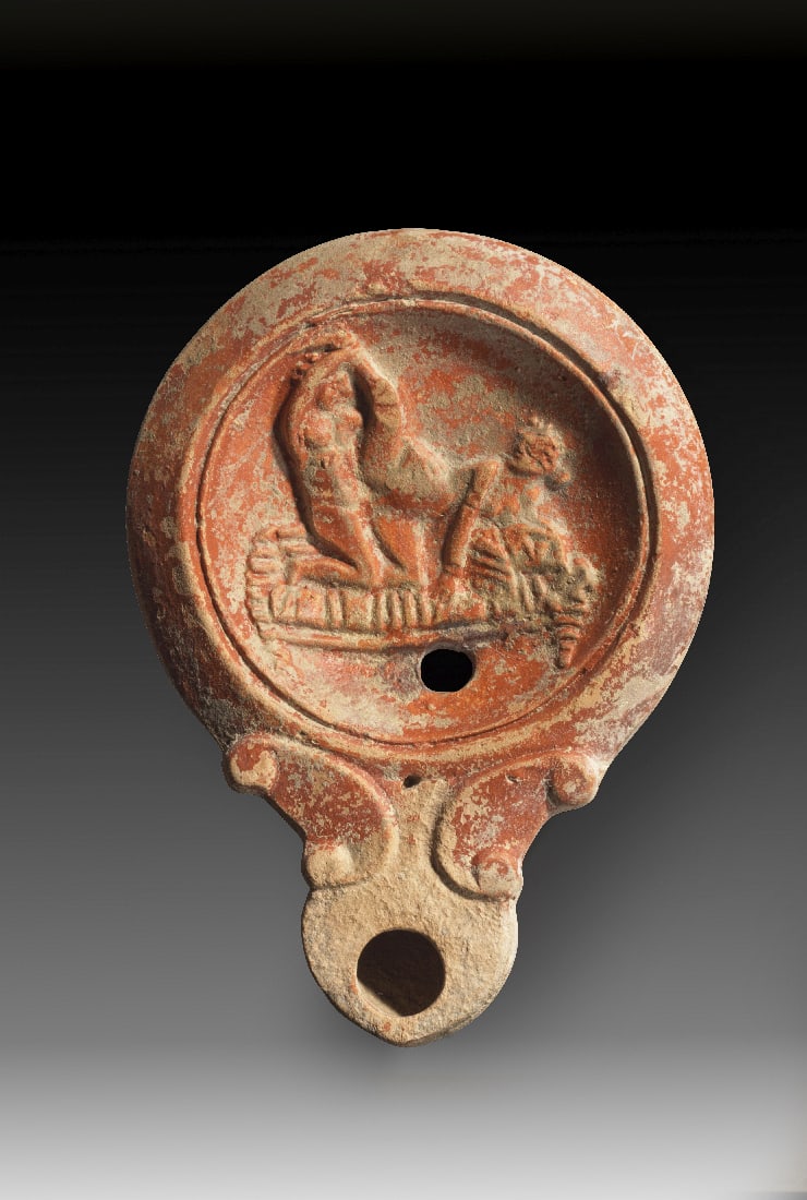 Tonlampe mit erotischer Szene.: Tonlampe mit erotischer Szene. Roemisch, spaetes 1. Jh. - fruehes 2. Jh. n. Chr. Loeschcke Typ IV, Schulter VIIb. L 11,5cm, B 8,5cm. Aus beigem Ton mit hellrotem ueberzug. Runder Corpus mit runder