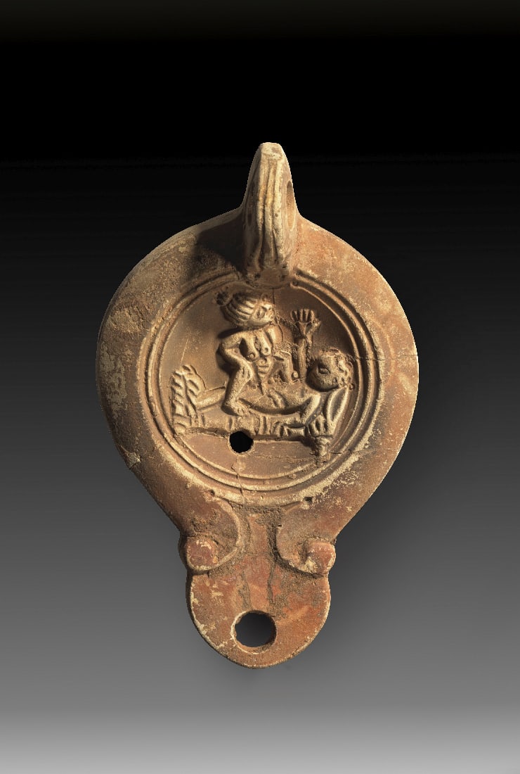 Tonlampe mit erotischer Szene.: Tonlampe mit erotischer Szene. Roemisch, spaetes 1. Jh. n. Chr. Loeschcke Typ IV, Schulter V. L 11,5cm, B 7cm. Aus beigem Ton mit braunem ueberzug. Runder Corpus mit runder Volutenschnauze mit rundem 
