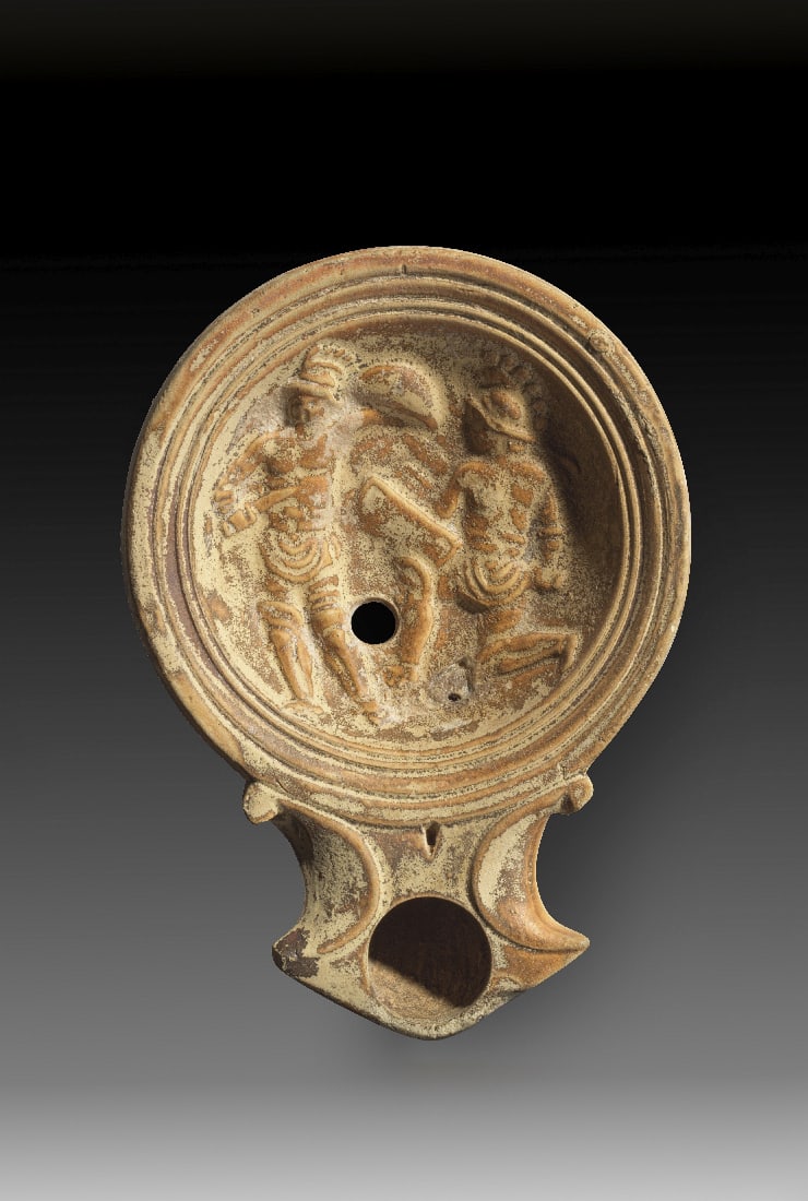 Tonlampe mit Gladiatorenpaar.: Tonlampe mit Gladiatorenpaar. Roemisch, 1. Jh. n. Chr. Loeschcke Typ Ic, Schulter Typ IIIa. L 11cm, B 8cm. Aus beigem Ton mit hellbraunem ueberzug. Runder Corpus mit eckiger Volutenschnauze mit rundem