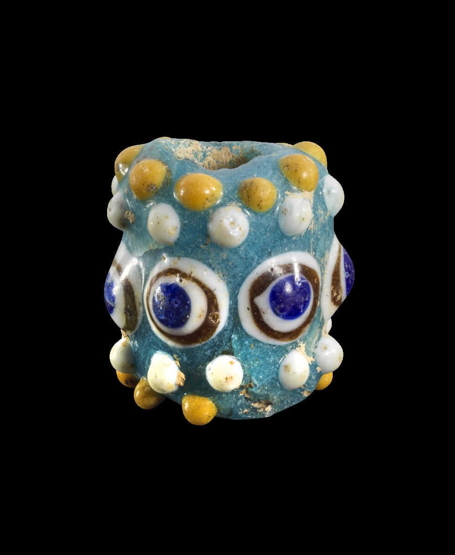 Grosse Glasperle mit Augen und Noppen.: Grosse Glasperle mit Augen und Noppen. Phoenizisch, 5. - 4. Jh. v. Chr. H 3,2cm, ? 2,9cm. Roehrenfoermig und aus hellblauem Glas, Noppen und Augen aus weissem, gelbem, braunem und dunkelblauem Glas.