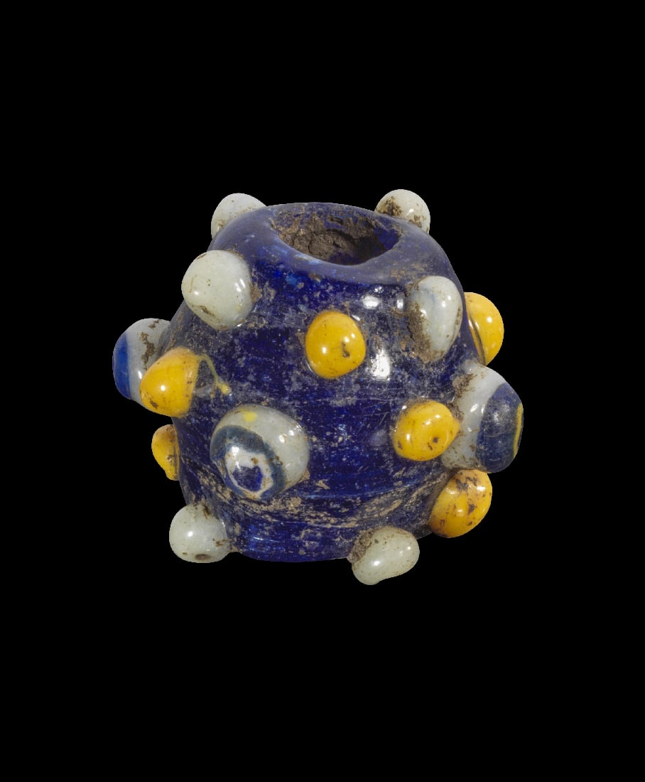 Grosse Glasperle mit Augen und Noppen.: Grosse Glasperle mit Augen und Noppen. Phoenizisch, 5. - 4. Jh. v. Chr. H 2,8cm, ? 3,4cm. Bikonisch und aus dunkelblauem Glas, Noppen und Augen aus weissem, gelbem und blauem Glas. Intakt.