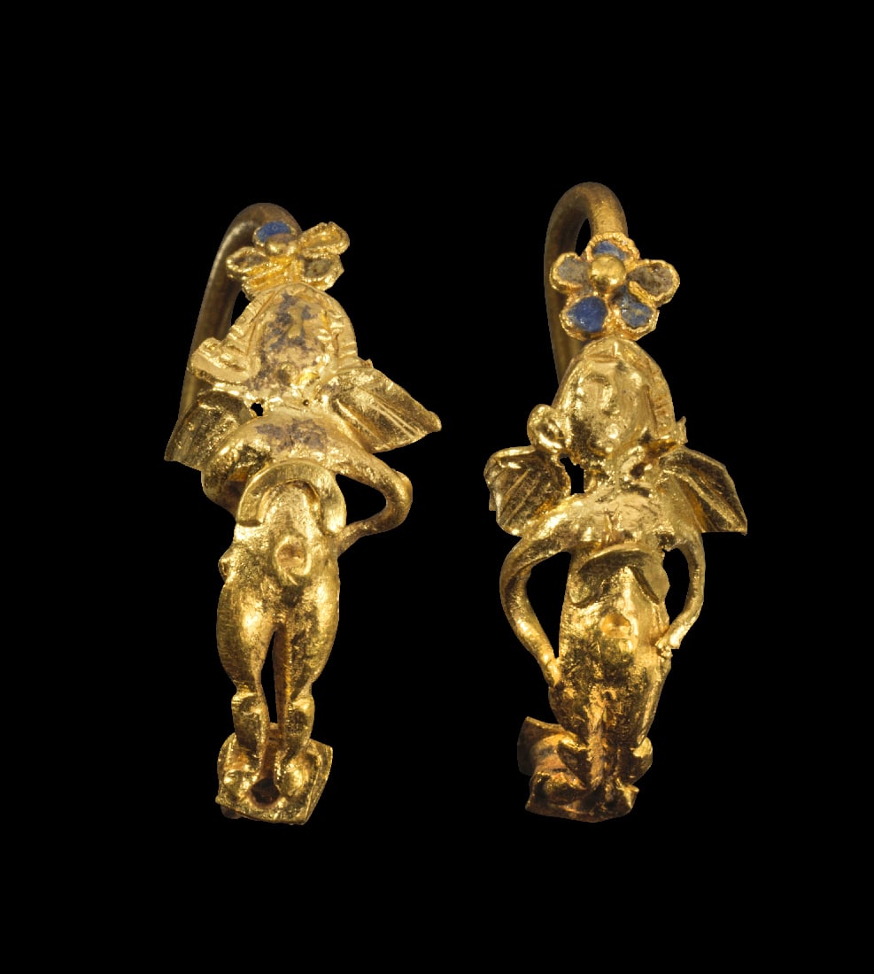 Paar goldene Erotenohrringe.: Paar goldene Erotenohrringe. Hellenistisch, 1. Jh. v. Chr. 2,96g, ? 2cm. Buegelohrringe mit einer kleinen Rosette, deren Bluetenblaetter mit blauem Email eingelegt sind. Daran anschliessend ein