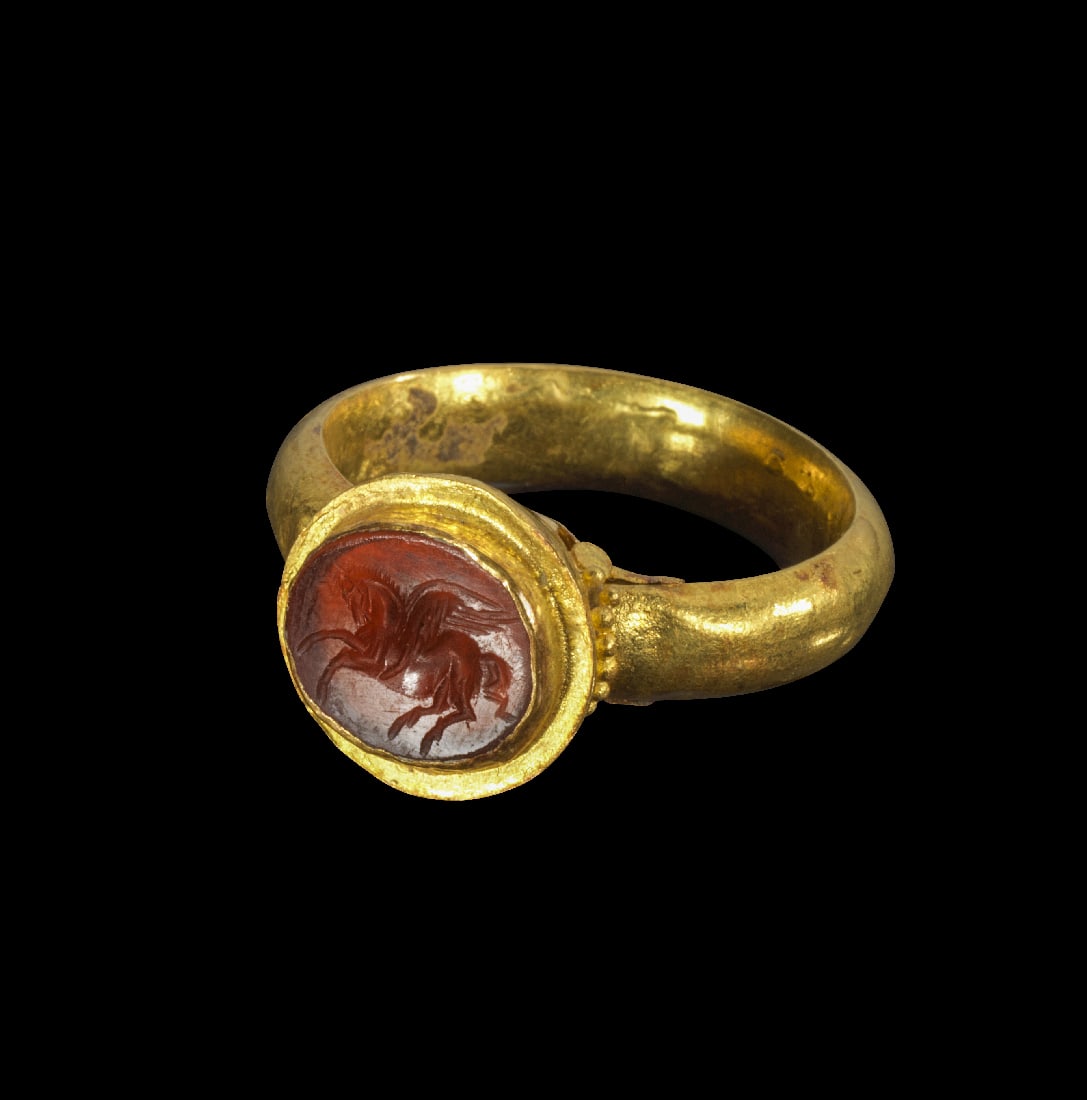 Goldring mit Karneol-Gemme.: Goldring mit Karneol-Gemme. Roemisch, 1. Jh. n. Chr. 5,07g, Ringgroesse 56. Gleichmaessig breite, hohle Schiene mit einer leicht konisch zulaufenden Fassung, in der ein runder, roter Karneol befestigt