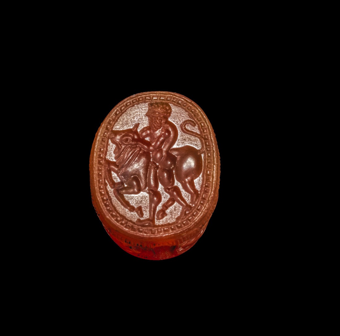 Etruskischer Skarabaeus aus Karneol mit Heraklesabenteuer.: Etruskischer Skarabaeus aus Karneol mit Heraklesabenteuer. 4. Jh. v. Chr. L 1,6cm. Oranger Karneol, laengsseits durchbohrt. Fein ausgearbeitete Details des Kaefers. Auf der Unterseite Intaglio mit
