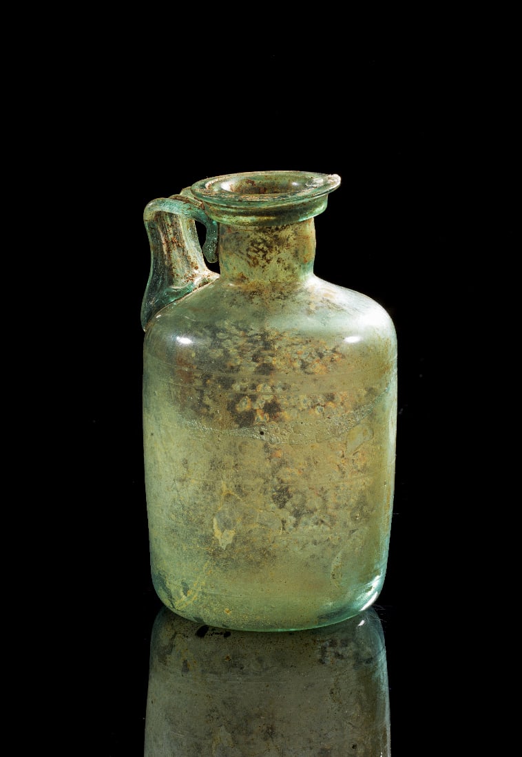 Roemischer Glaskrug mit eingeritzten Parallelrillen.: Roemischer Glaskrug mit eingeritzten Parallelrillen. Roemisch, 1. - 2. Jh. n. Chr. H 13cm. Freigeblasener Krug aus transluzidem, leicht gruenlich bis blaeulich getoentem Glas. Der bauchige Korpus ist 