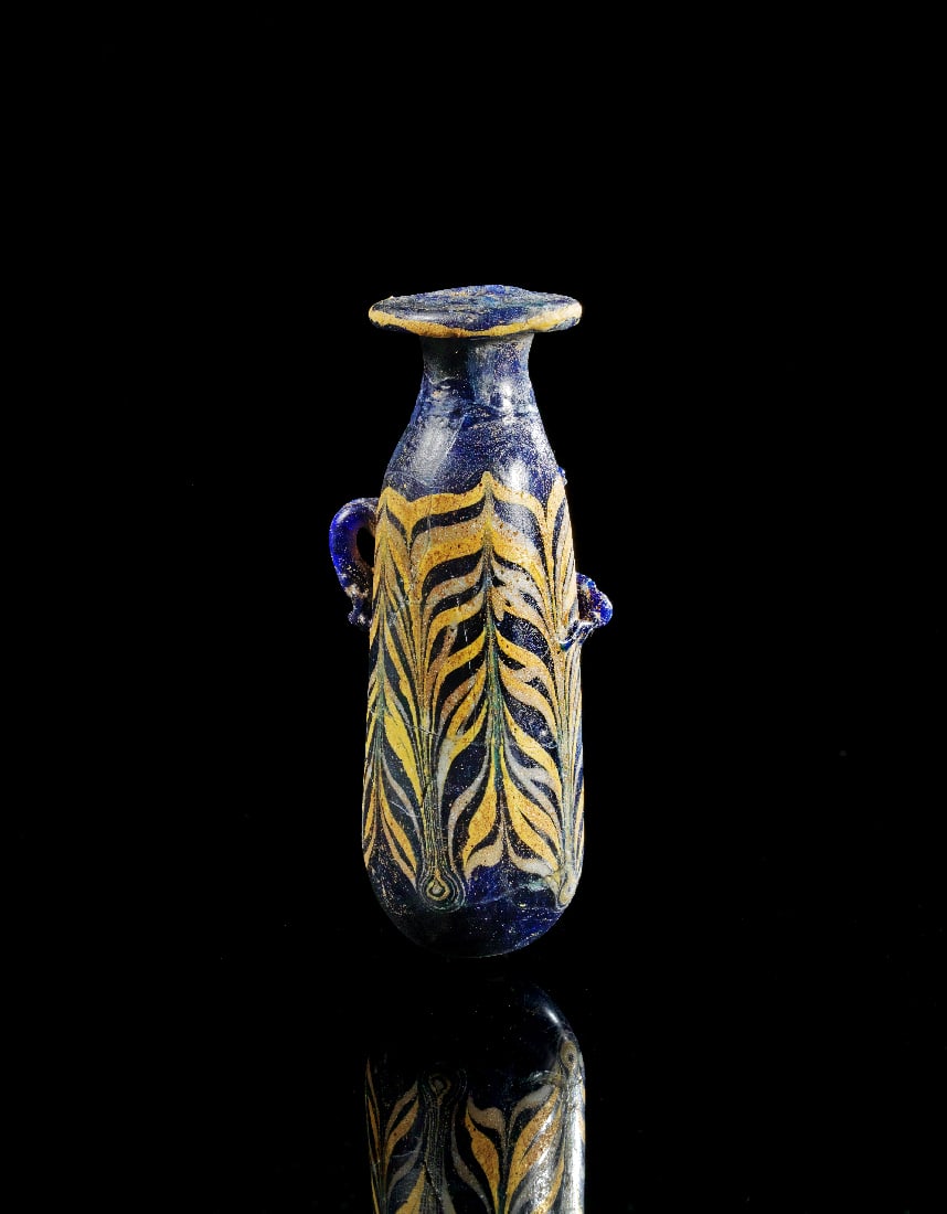 Alabastron in Sandkerntechnik.: Alabastron in Sandkerntechnik. oestlicher Mittelmeerraum, ca. 4. Jh. v. Chr. H 9,5cm. Laengliches Gefaess aus opakem, dunkelblauen Glas mit seitlichen oesen. Vom Hals ausgehende gelbe und weisse Faede