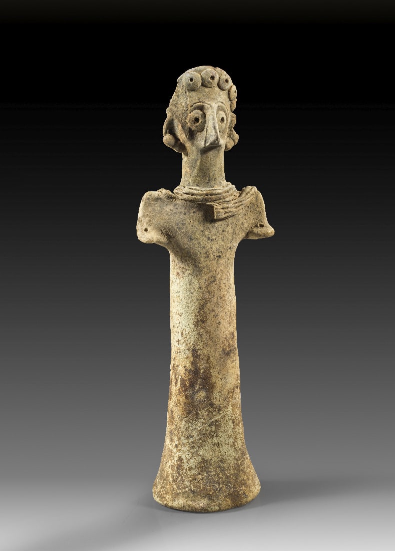 Idol.: Idol. Syro-hethitisch, Mitte 2. Jt. v. Chr. ? 18,4cm. Hellbeiger Ton. Saeulenfoermiger Koerper mit breiten Schultern und vorgestreckten Stummelarmen. Der Kopf mit Vogelnase und Locken aus Tonlinsen