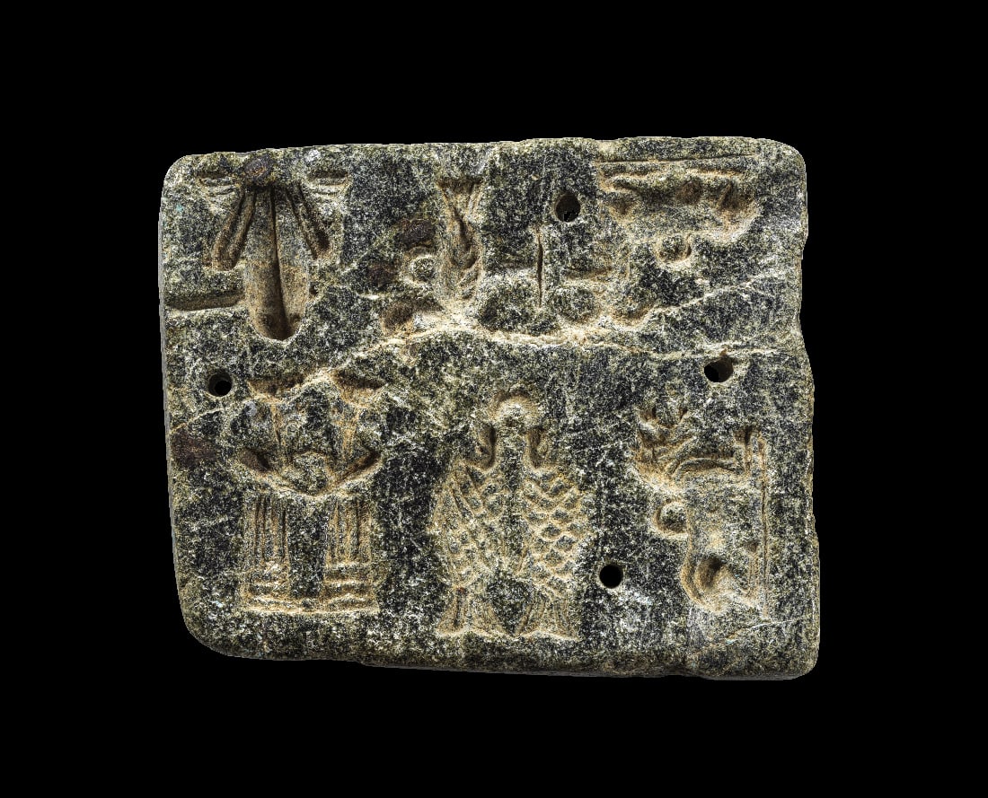 Sumerische Treib- oder Gussform.: Sumerische Treib- oder Gussform. 3. Jt. v. Chr. Schwarzer Stein. 7, 8 x 6,3 x 1,3cm. Etwas unregelmaessige Steinplatte mit vertieften Reliefs: doppelter Fisch, doppelte baertige Gottheit, ein Frosch,