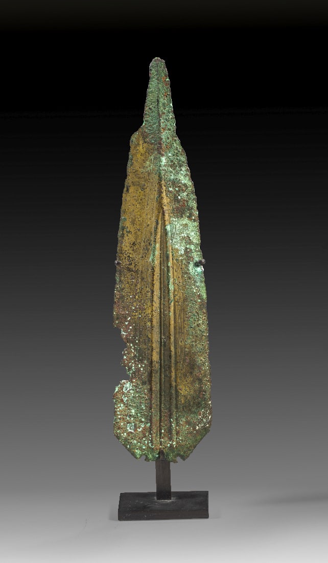 Schoene Lanzenspitze aus Bronze.: Schoene Lanzenspitze aus Bronze. Luristan, 1200 - 800 v. Chr. L 26,1cm, B 6,4cm, H mit Staender 29,3cm. Sehr breites zweischneidiges Blatt mit wunderschoener lanzettfoermiger Blutrinne, die seitlich v