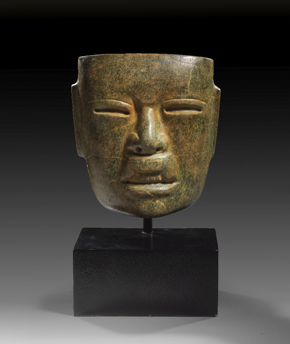 Maske.: Maske. Olmeken, ca. 900 - 400 v. Chr. H 17cm, L 16cm. Nephrit. Glatte Oberflaeche. Gesicht mit mandelfoermigen Augen, grosser Nase, dicken Lippen und gebleckten Zaehnen. Zwei Bohrloecher unterhalb der