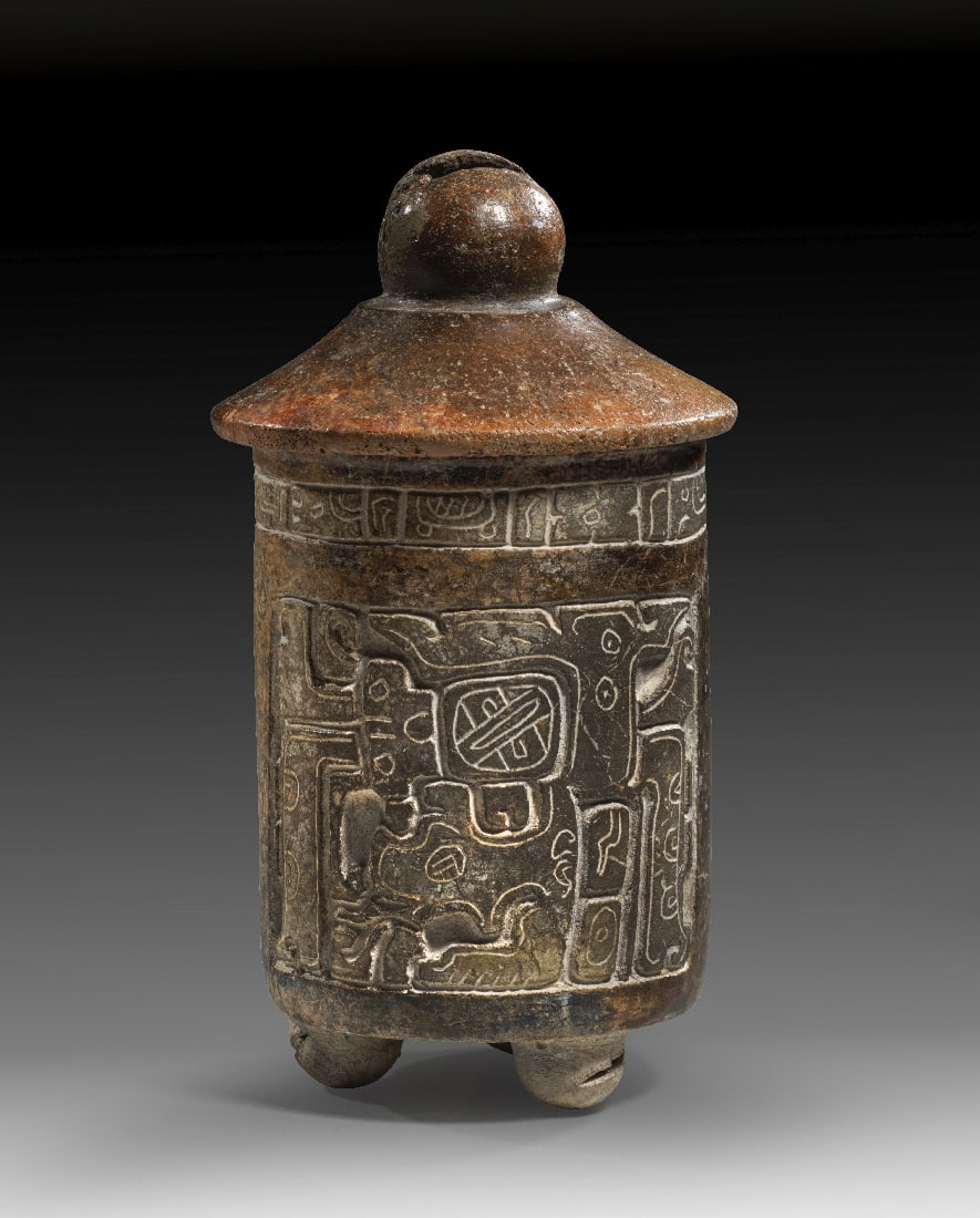 Cache-Gefaess mit Deckel und Darstellung des Gottes K'awiil.: Cache-Gefaess mit Deckel und Darstellung des Gottes K'awiil. Maya-Kultur, Fruehklassische Periode, ca. 500 - 600 n. Chr. H 23,5cm ? (Deckel) 12,5cm. Das reich mit geschnitzten Bildern verzierte