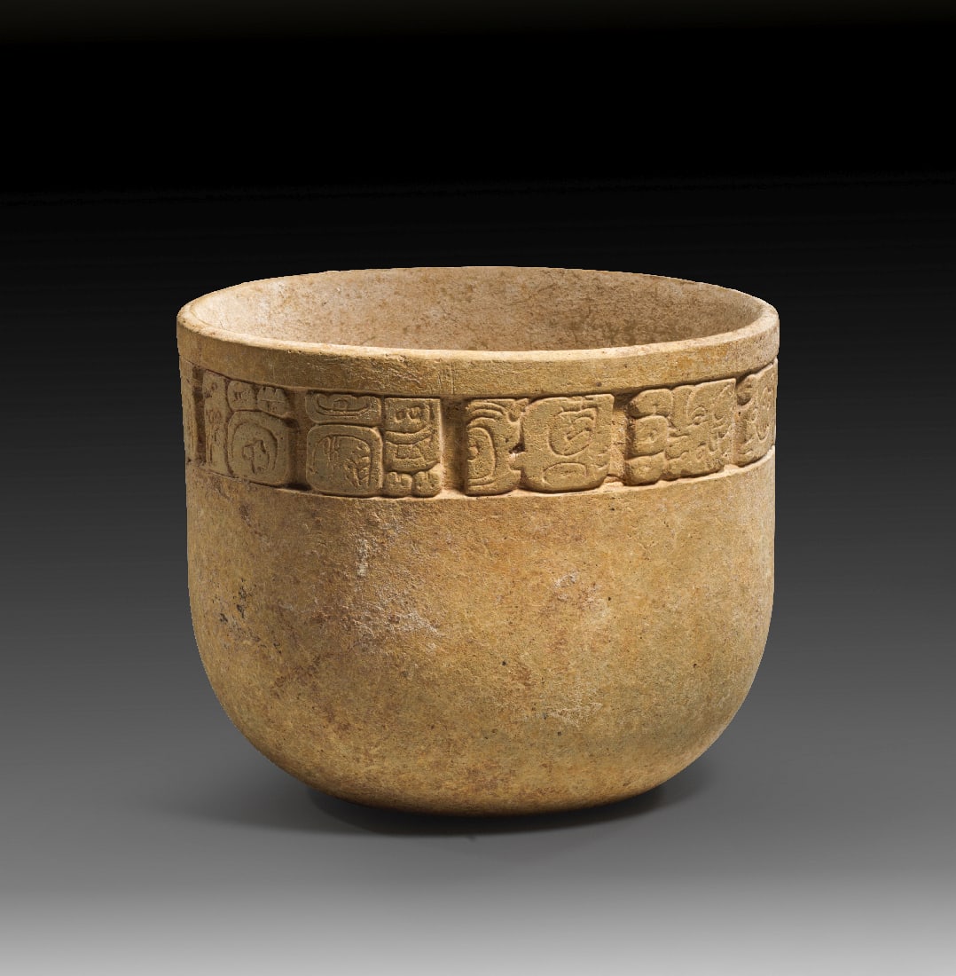 Hoher Becher mit Glyphen.: Hoher Becher mit Glyphen. Maya-Kultur, Klassische Periode, ca. 600 - 900 n. Chr. H 11,4cm ? 14cm. Beiger Ton. Gerade Wandung und leicht eingewoelbter Fuss. Unterhalb der Lippe ein Fries mit