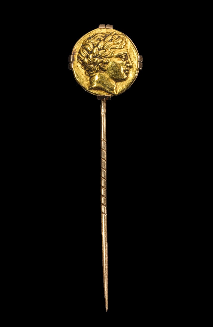 Anstecknadel mit Nachguss einer antiken, griechischen Muenze.: Anstecknadel mit Nachguss einer antiken, griechischen Muenze. 13,48g, L 7,6cm. Spitz zulaufender Schaft mit spiraligen Einkerbungen und einer Punze. Der Kopf besteht aus dem Nachguss (?) von einem