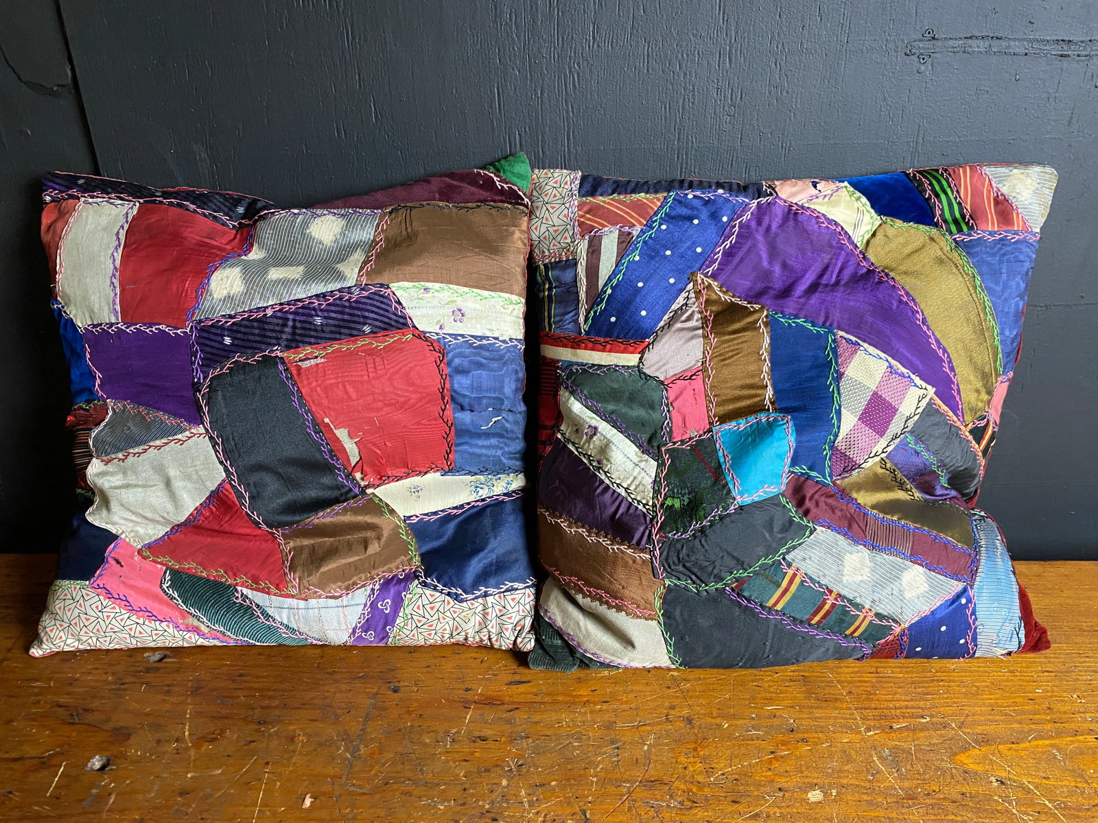A Pair of Antique/Vintage Crazy Quilt Patchwork Pillows: A pair of decorative throw pillows crafted in a "crazy quilt" patchwork style. Each pillow features numerous irregularly shaped fabric scraps, predominantly silk, satin, velvet, and possibly cotton, i