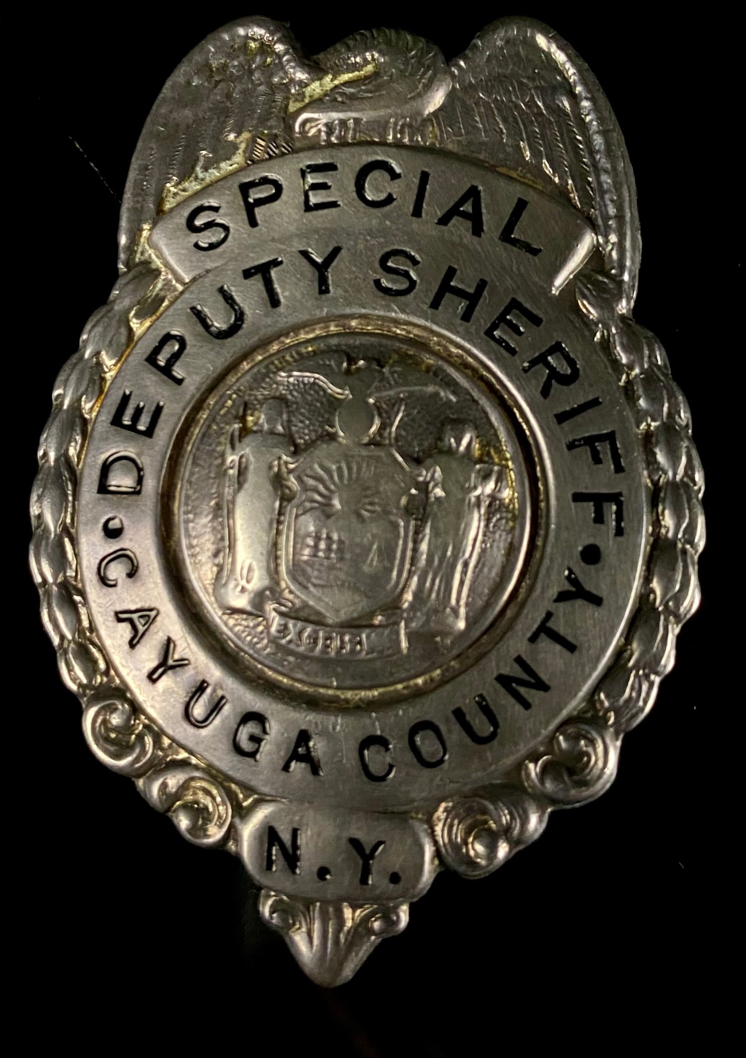 Harvey's Syracuse Sterling Silver Special Deputy Sheriff Badge, Cayuga County, N.Y.: A circular law enforcement badge, primarily silver-toned metal, identified as sterling silver. The design features an eagle at the top with spread wings framing a central circular motif. The front is 