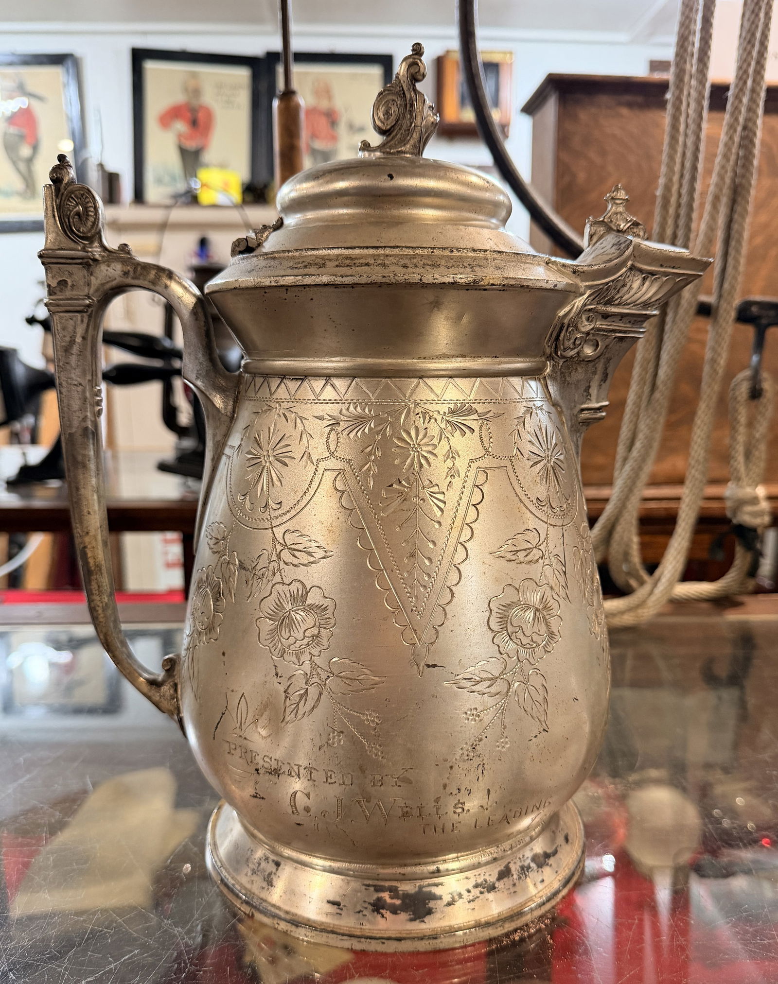 Inscribed for 1888 Oneida Fireman's Convention Presented by CJ Wells: An Antique Victorian Meriden Silver Plate Water Pitcher. This lidded metal pitcher or ewer presents an ornate late 19th-century aesthetic with elaborate engraved decoration including floral sprays,