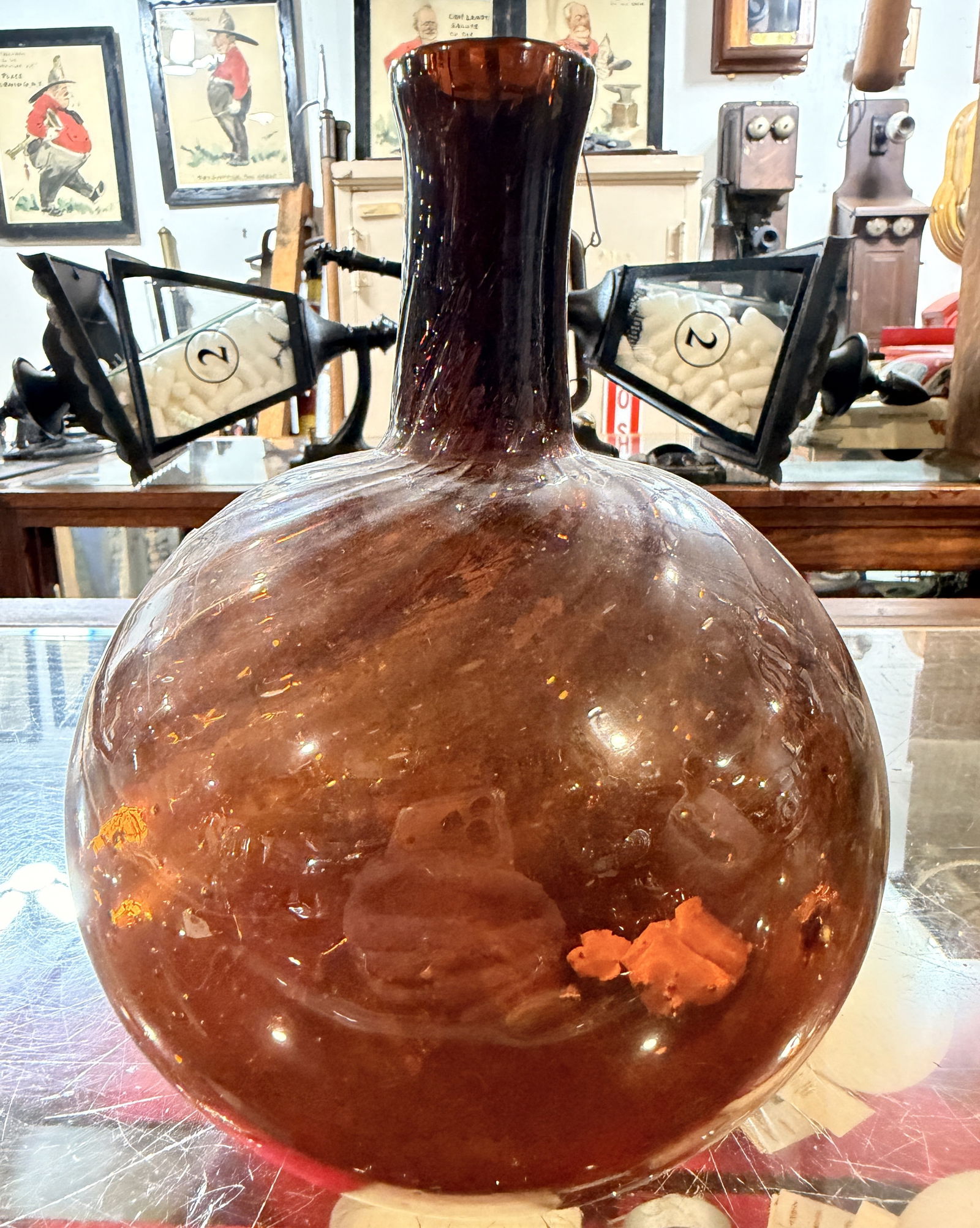 An Antique 19th Century Handblown Amber Glass Fire Bottle: An Antique 19th Century Handblown Amber Fire Bottle. This large, globular glass bottle is crafted from dark amber or dark brown glass, featuring a spherical body that tapers to a short, slightly