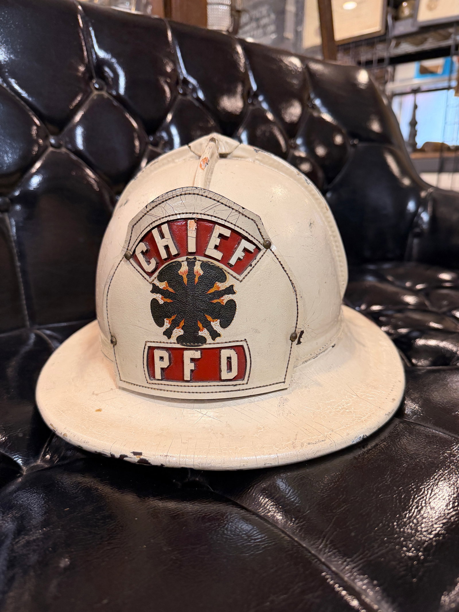 Vintage American Cairns & Brother Leather Chief Firefighter Helmet: A vintage War Baby American Cairns & Brother leather chief firefighter helmet, commonly referred to as a "leatherhead," featuring a classic broad-brimmed design and a white painted finish. The front i