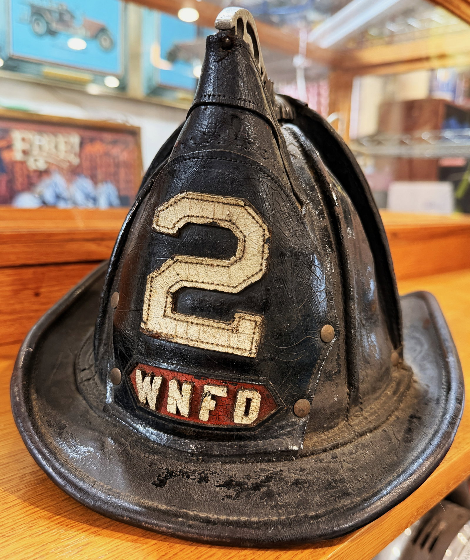 Cairns & Brothers Leather Fireman's Helmet with '2' and 'WNFD' Badge (West Nyack NY): A Cairns & Brothers leather fireman's helmet, constructed primarily of black leather with a heavily lacquered or shellacked finish. It features a wide brim, a ribbed dome, and a decorative, scrolled m