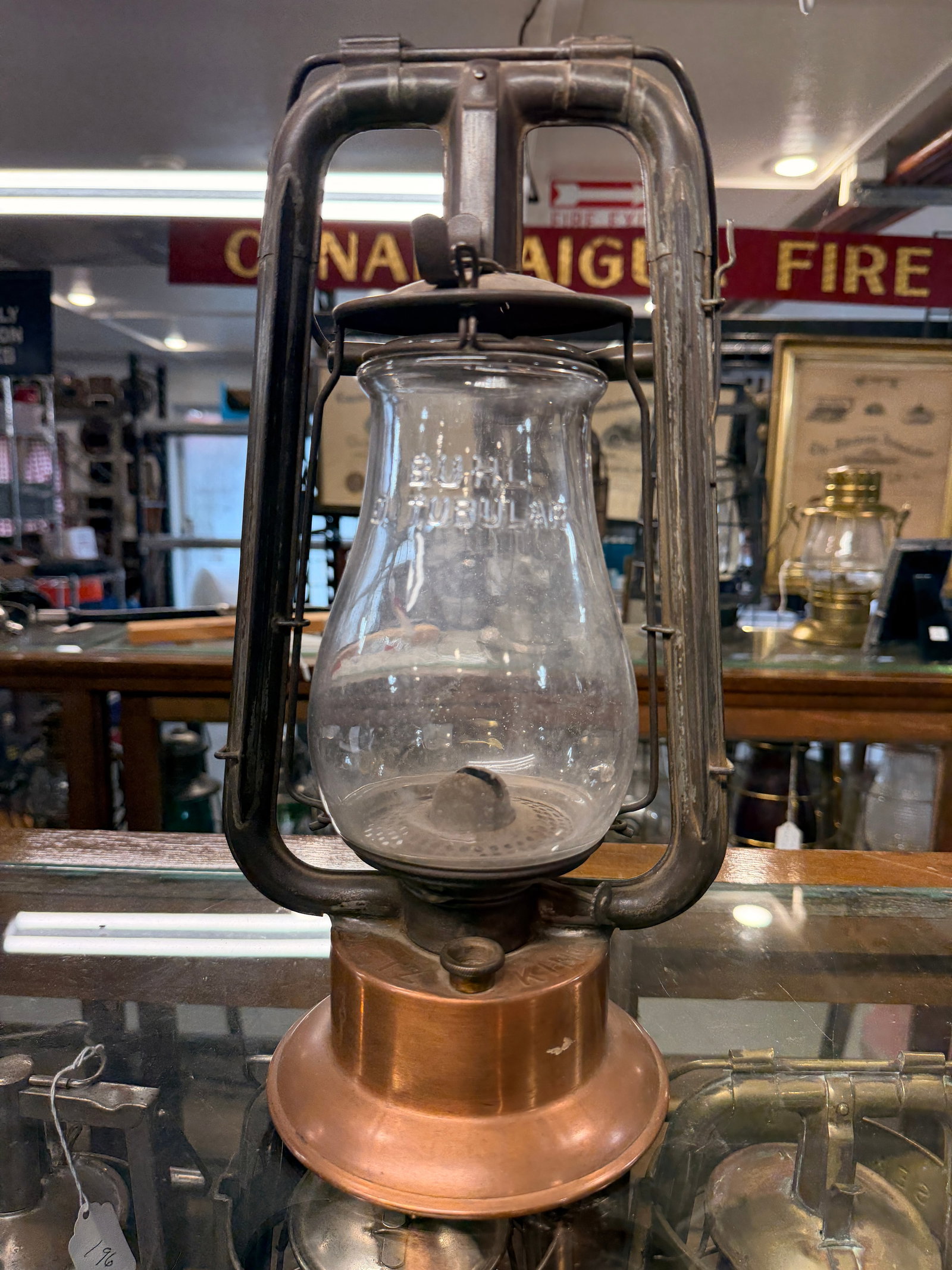 Antique Tubular Kerosene Lantern with Dietz Fire King Globe and 'Fire Dept' Copper Fount: An antique tubular kerosene lantern, featuring a patinated dark metal frame and a copper fuel fount. The copper fount is clearly embossed "FIRE DEPT" (Fire Department), suggesting a historical affilia
