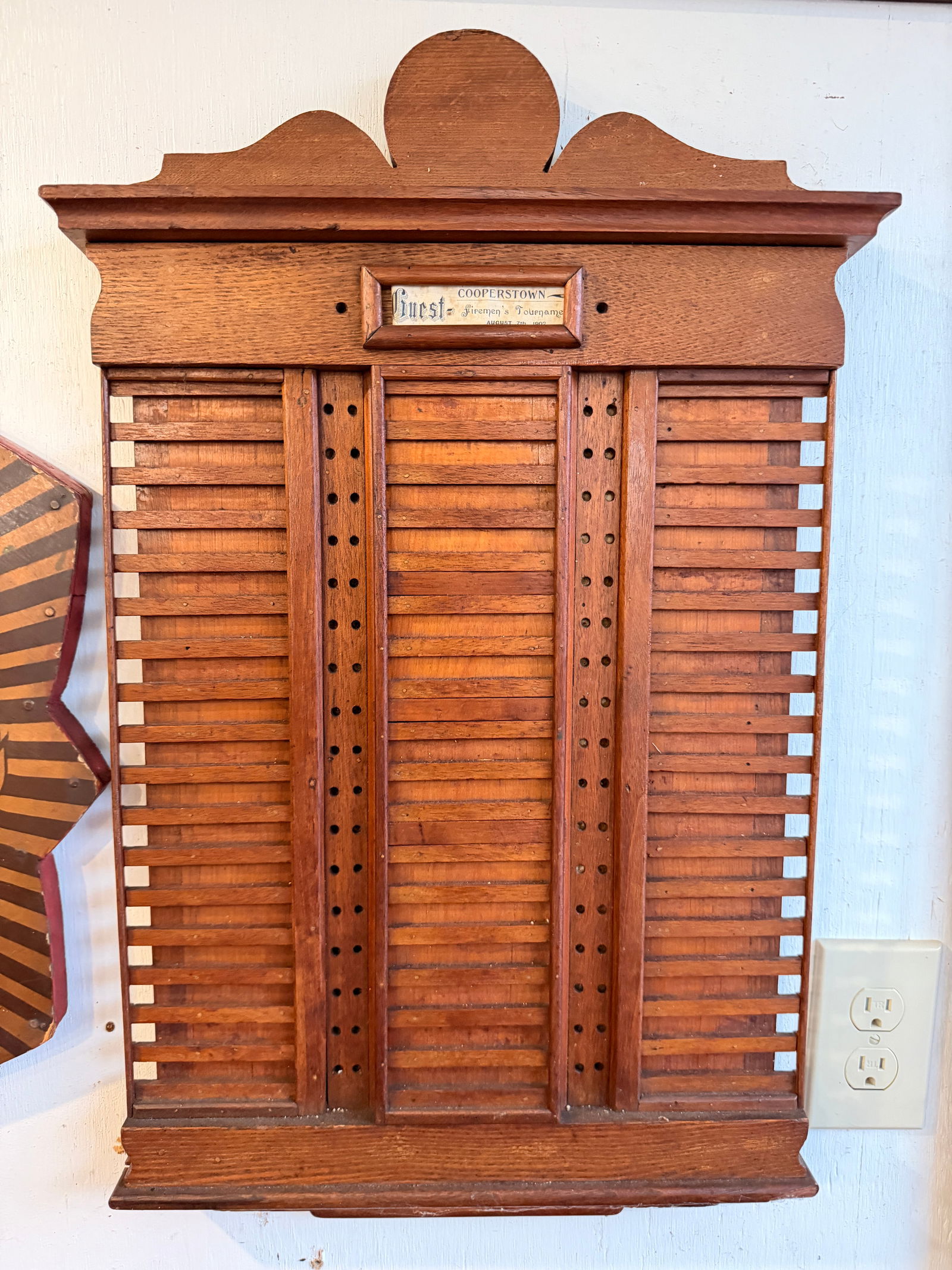 Early 20th Century Oak Cooperstown Firemen's Tournament Scoreboard, 1902: An early 20th-century dark-stained hardwood board, likely oak, designed to function as a score or display rack. The piece exhibits a utilitarian style with a modest decorative scrolled top and bottom
