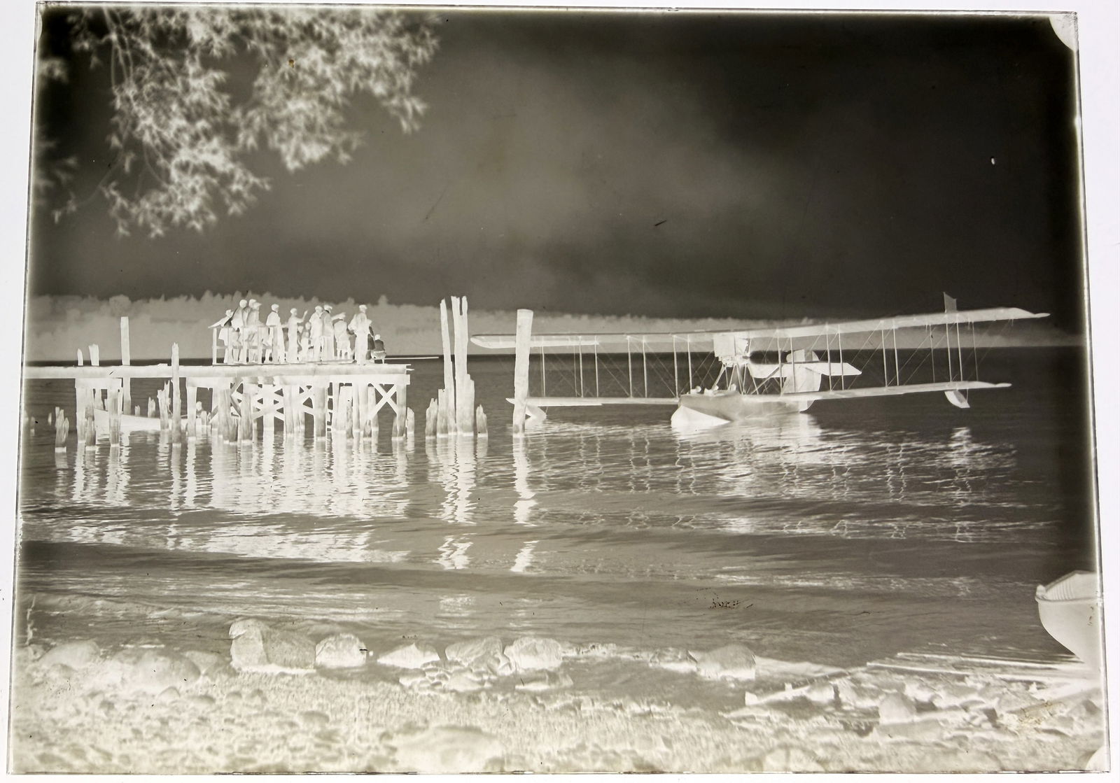 Early 20th Century Large Format Glass Plate Negative of a Biplane Seaplane: An archival, large format photographic glass plate negative, likely dating to the early 20th century. The monochrome image depicts an early biplane floatplane (seaplane) resting on the water adjacent