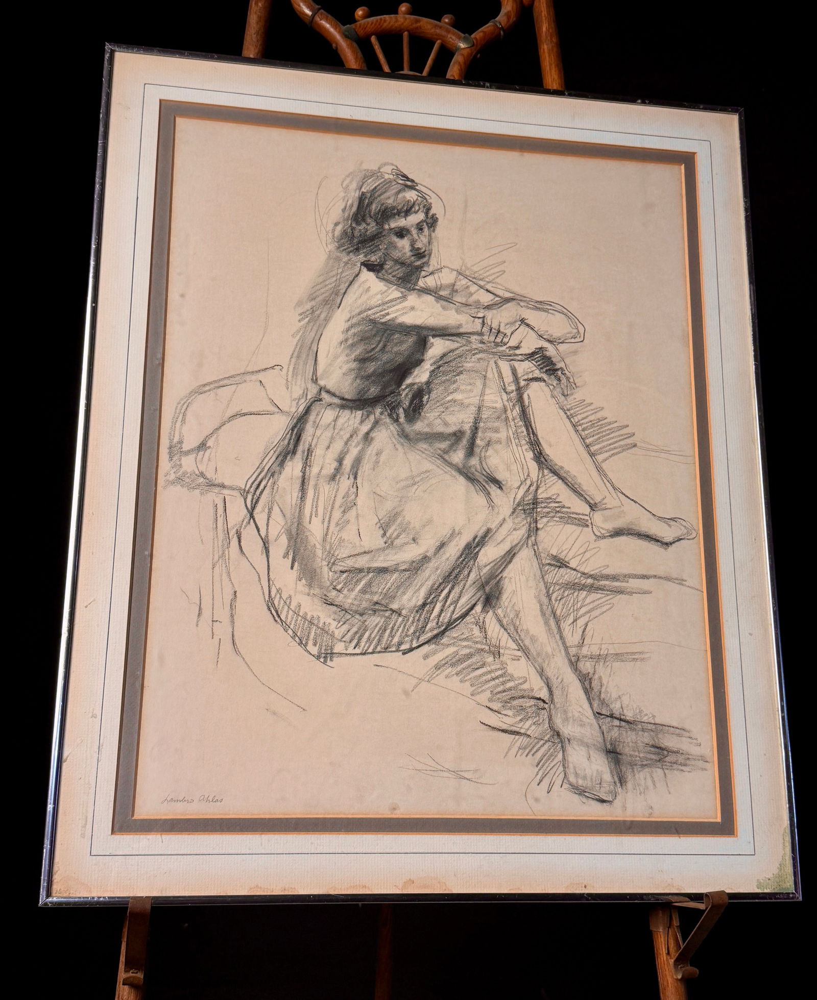 Lambro Ahlas Charcoal Drawing of a Seated Female Model: A single framed expressive figurative drawing executed in charcoal or graphite on light-toned paper. The artwork depicts a seated female figure resting with crossed arms and legs, rendered in a modern