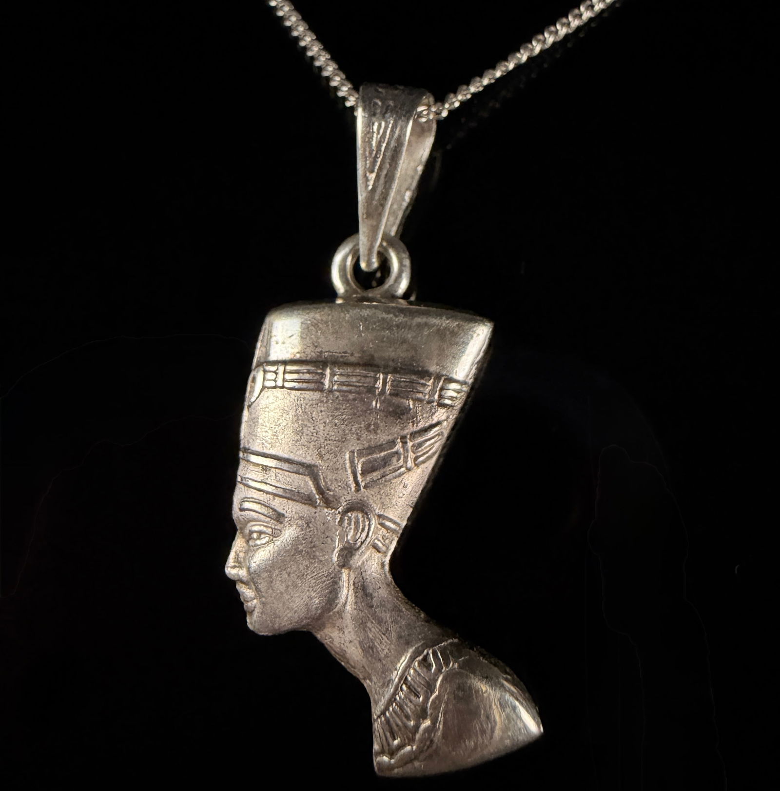 Sterling Silver Queen Nefertiti Bust Pendant Necklace: A sterling silver necklace in the Egyptian revival style featuring a pendant depicting the profile bust of Queen Nefertiti. The cast pendant displays the queen's iconic crown and jewelry. The pendant