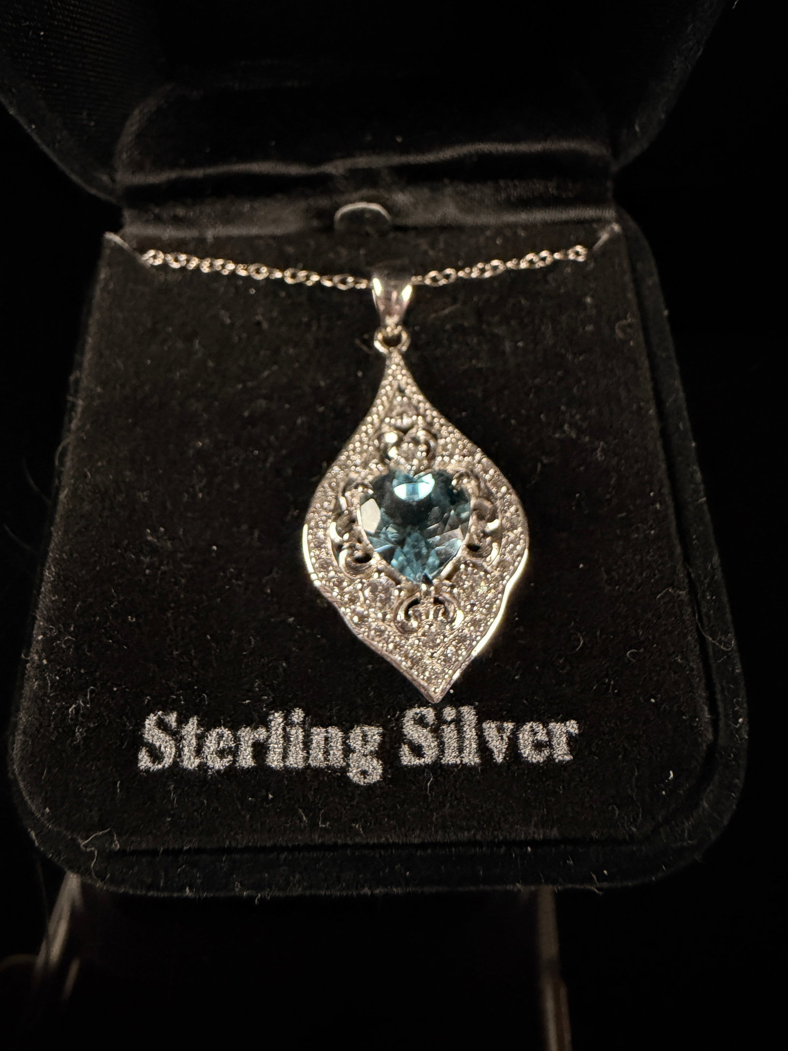 Sterling Silver Heart Cut Blue Topaz and White CZ Pendant Necklace: This contemporary sterling silver necklace features an ornate openwork pendant in an elongated leaf shape. The piece is centered with a faceted heart-cut blue topaz gemstone, framed by a decorative bo