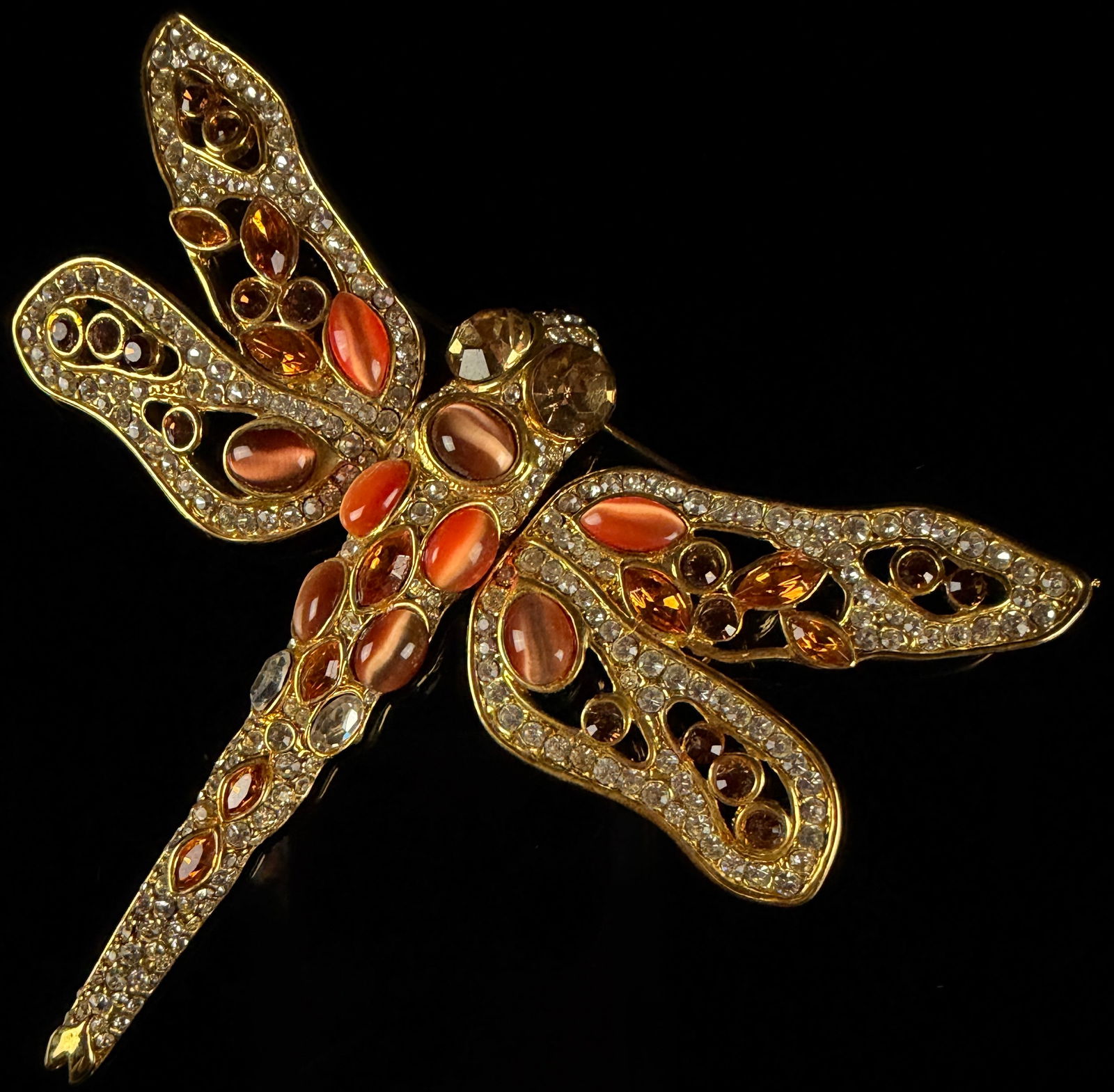 A Gold-Tone and Multi-Stone Dragonfly Brooch: This dragonfly brooch is constructed from gold-tone metal and features an elaborate arrangement of multi-colored stones. The insect form includes large faceted champagne-colored stones representing th