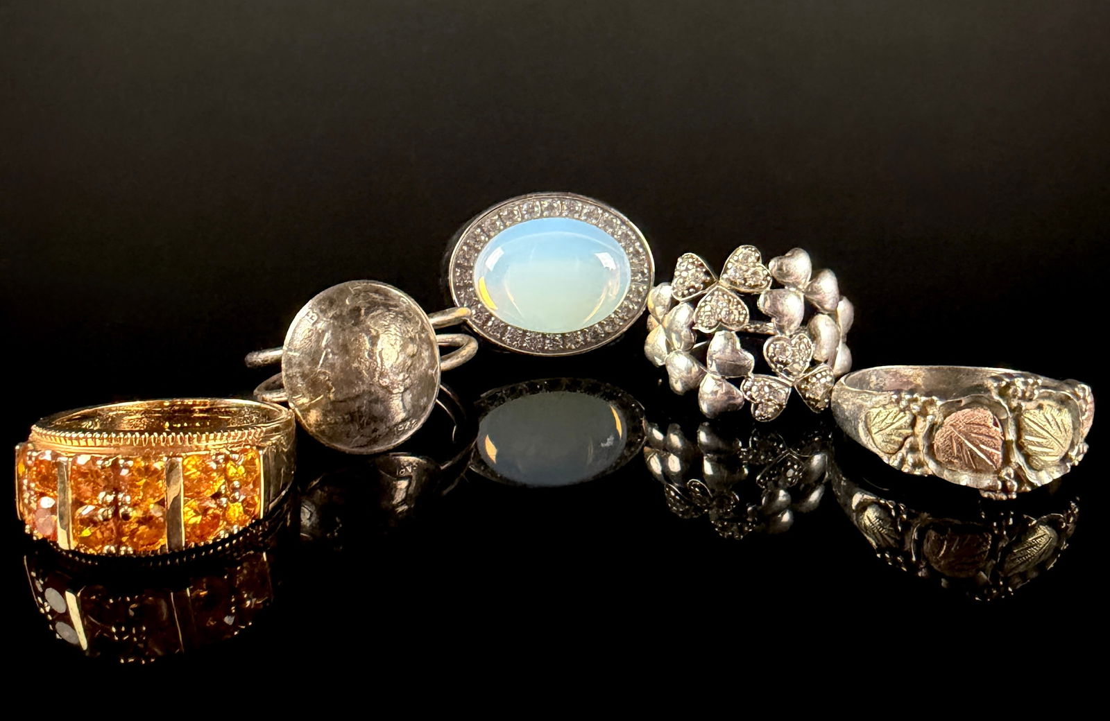 A Collection of Sterling Silver and Gold-Toned Costume Rings: An assortment of rings featuring various designs and materials. The group includes a wide gold-toned band pav?©-set with numerous faceted orange stones, a multi-heart motif ring marked Ireland, and a